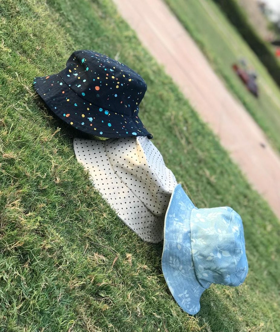 Three bucket hats arranged on grass: black speckled, white dotted, and light blue denim.