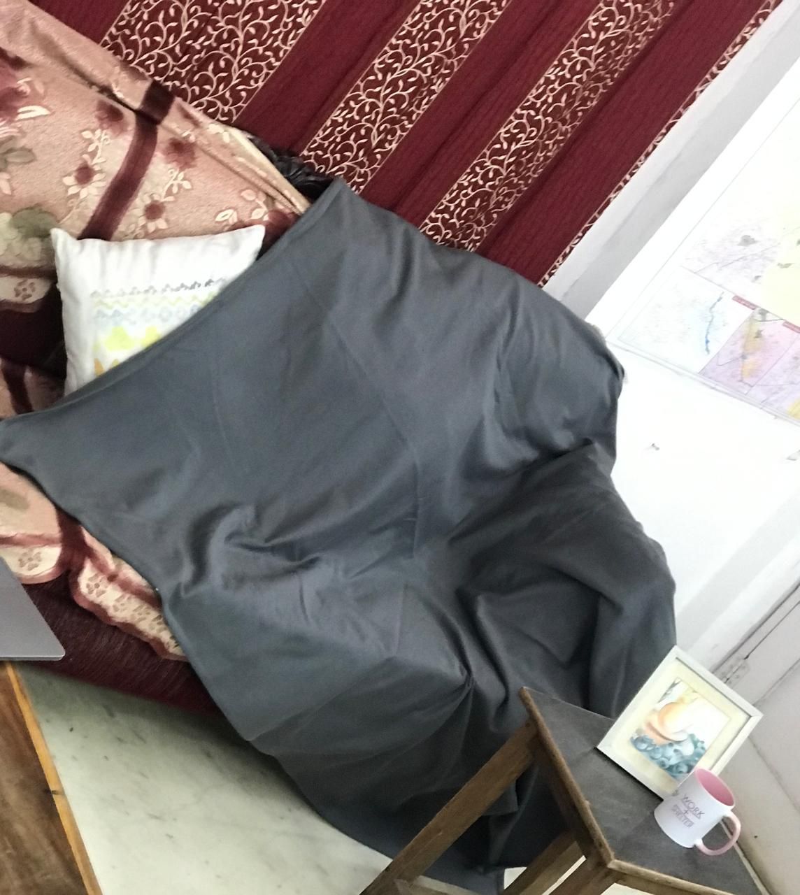 Person sitting on bed with burgundy patterned bedding, holding dark gray pillow.