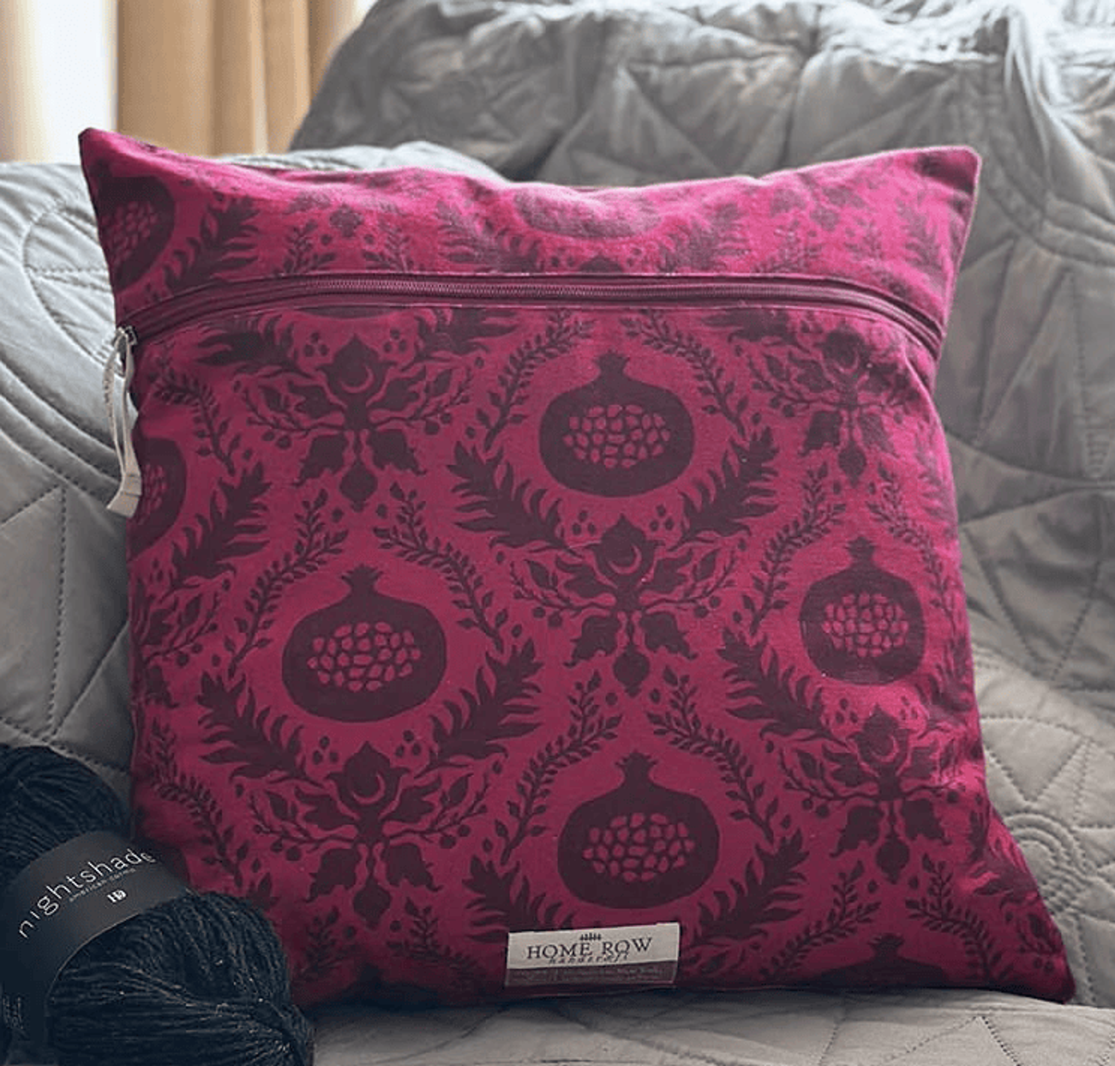 Magenta damask decorative pillow on bed with gray quilted bedding and pillows.