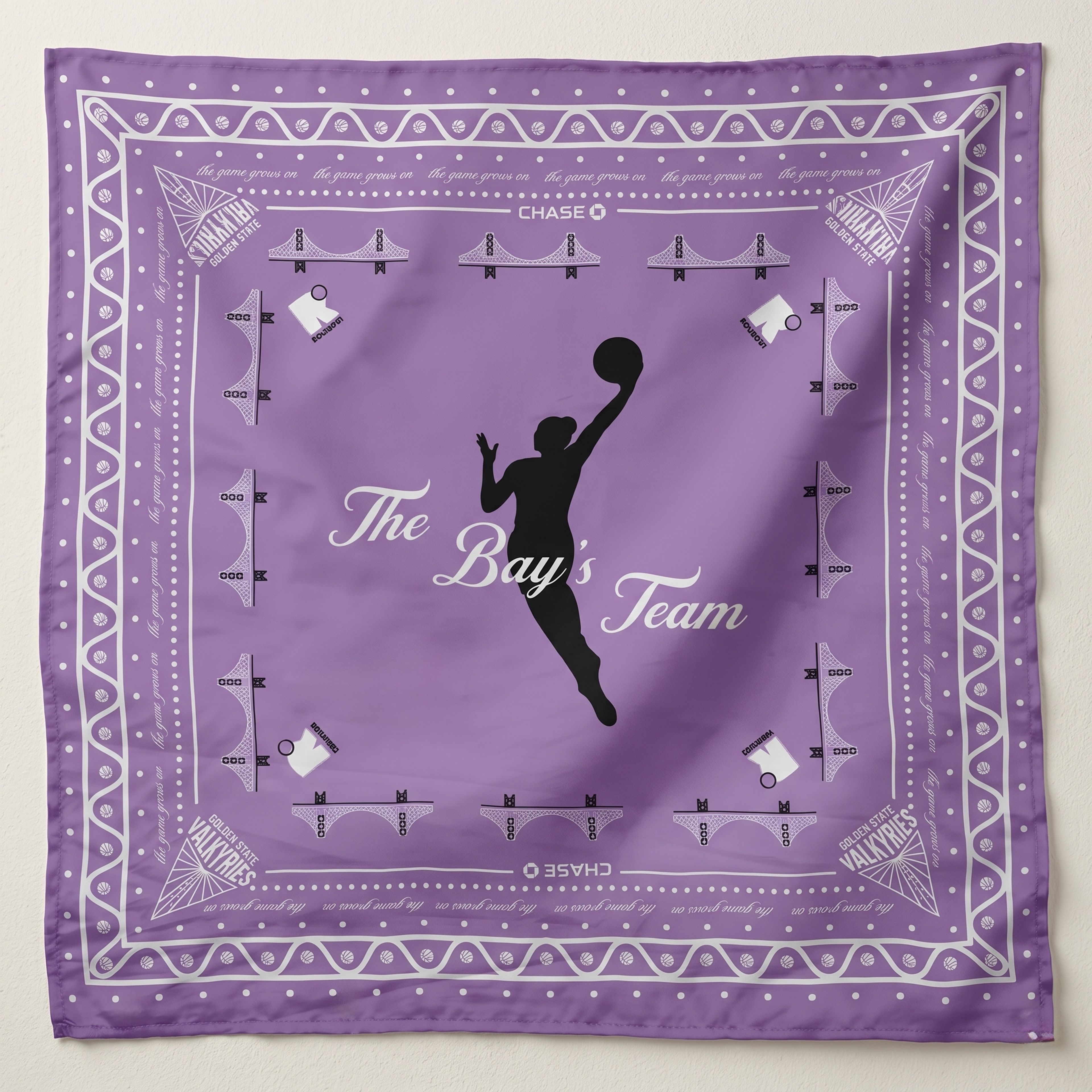 Lavender silk scarf featuring a black silhouette of a female basketball player dunking, titled 'The Bay's Team.' The design includes white Golden Gate Bridge icons, Golden State Valkyries logos in the corners, and a decorative patterned border."