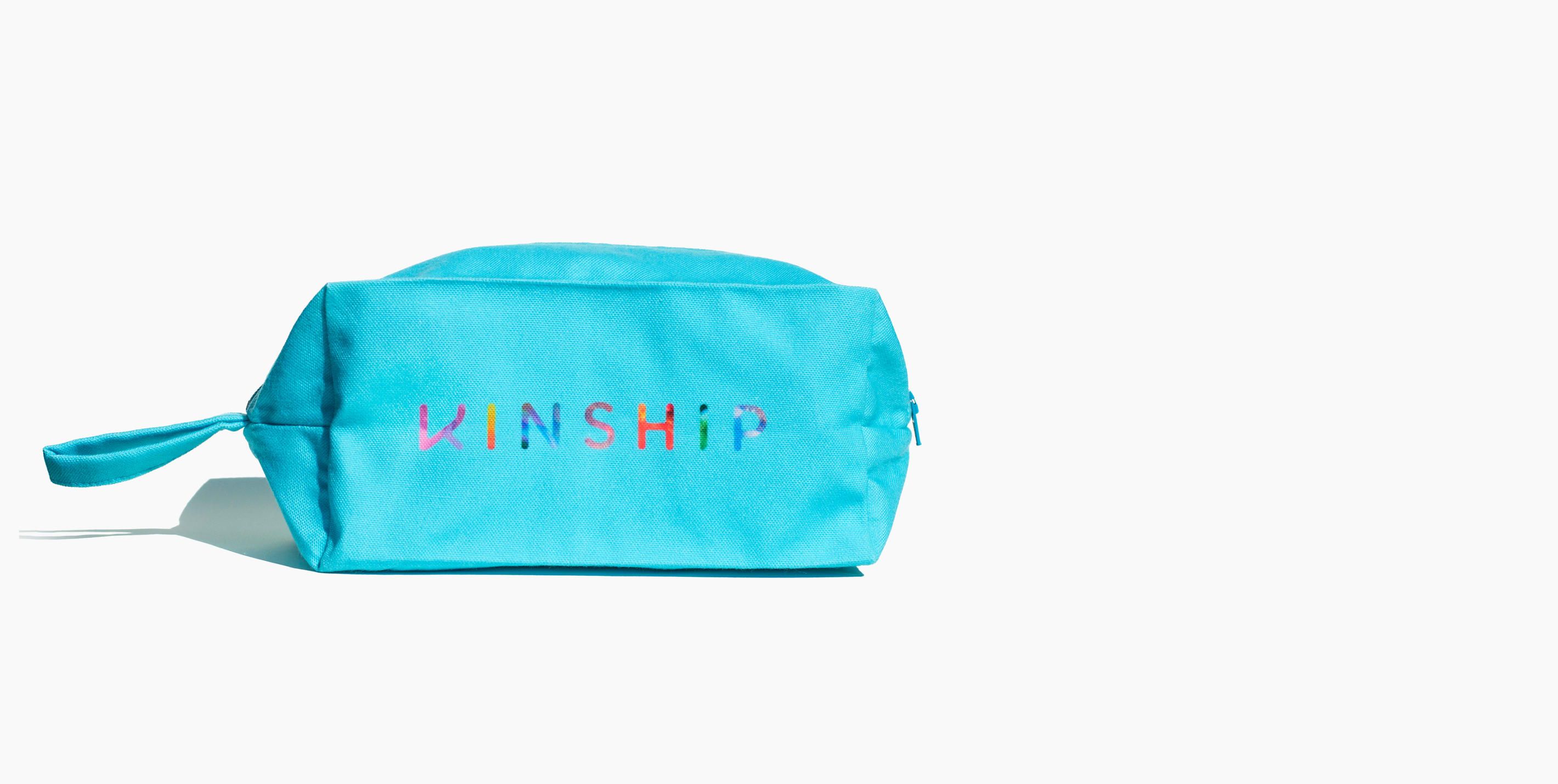 Bright turquoise KINSHIP cosmetic bag with colorful embroidered text and wrist strap.