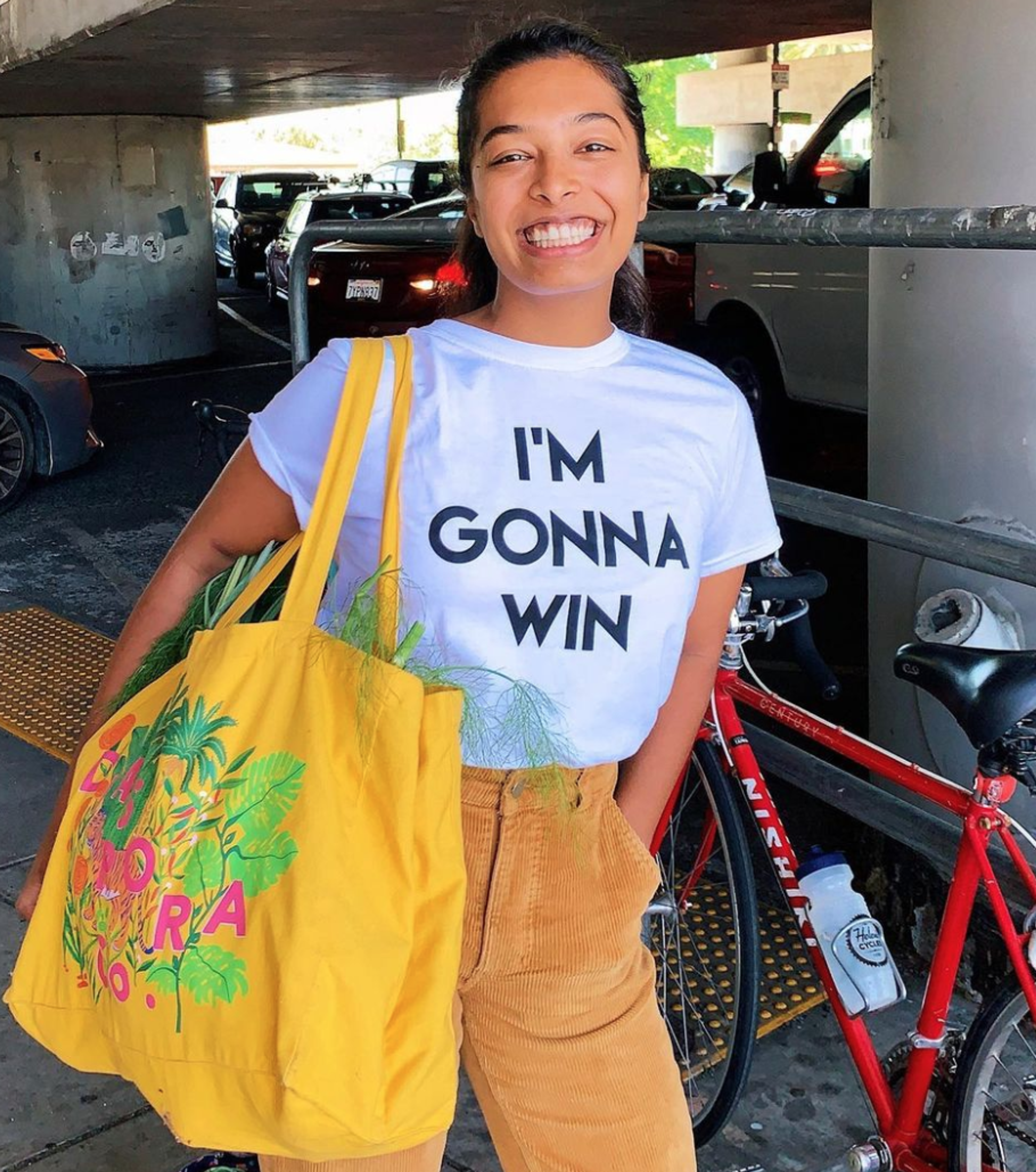 Woman smiling in parking garage wearing "I'm Gonna Win" shirt and yellow tote bag.