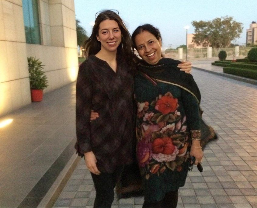 Two smiling women posing together on a paved outdoor pathway near modern buildings.