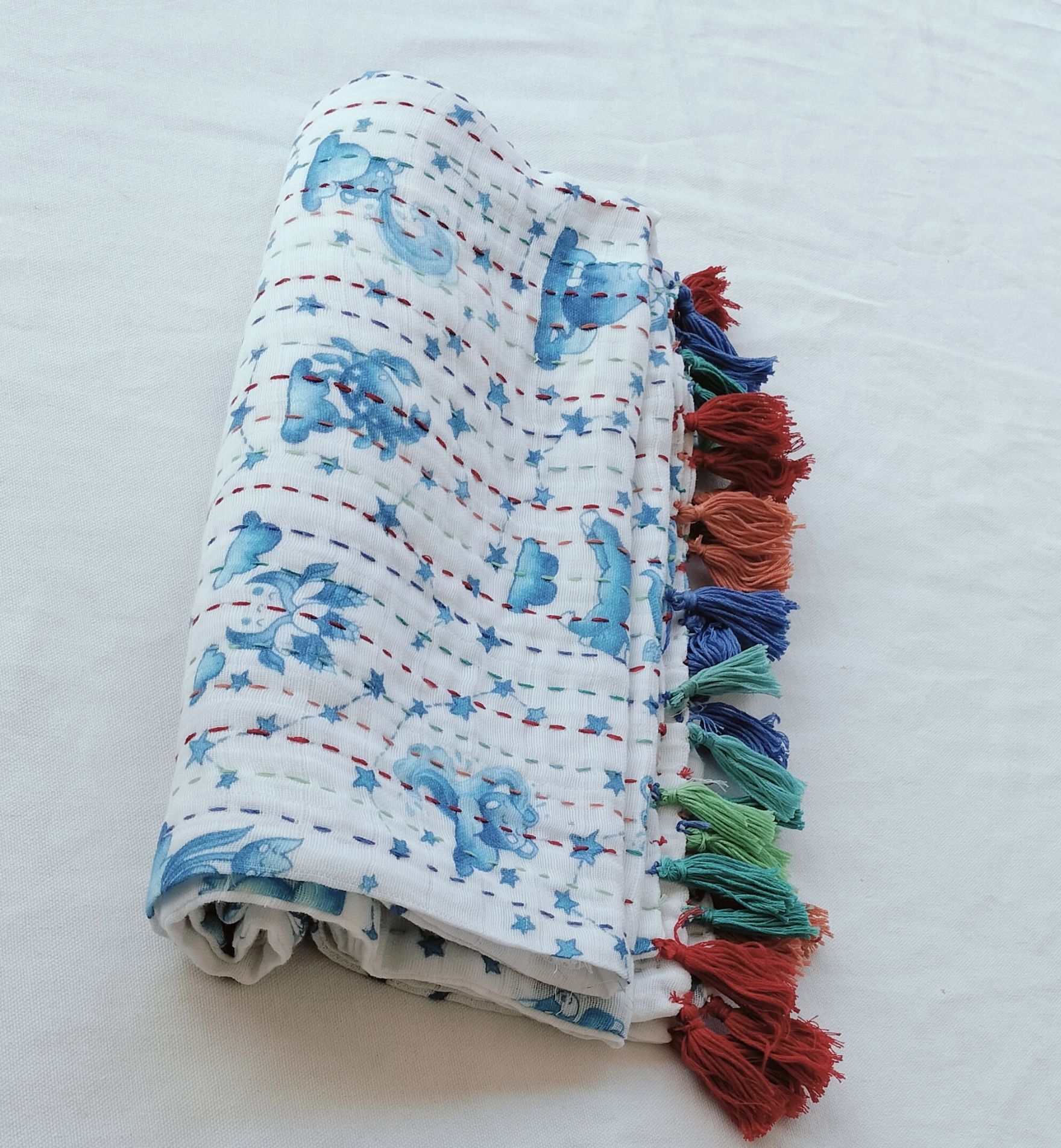 Rolled white fabric with blue fish pattern and colorful decorative tassels attached.