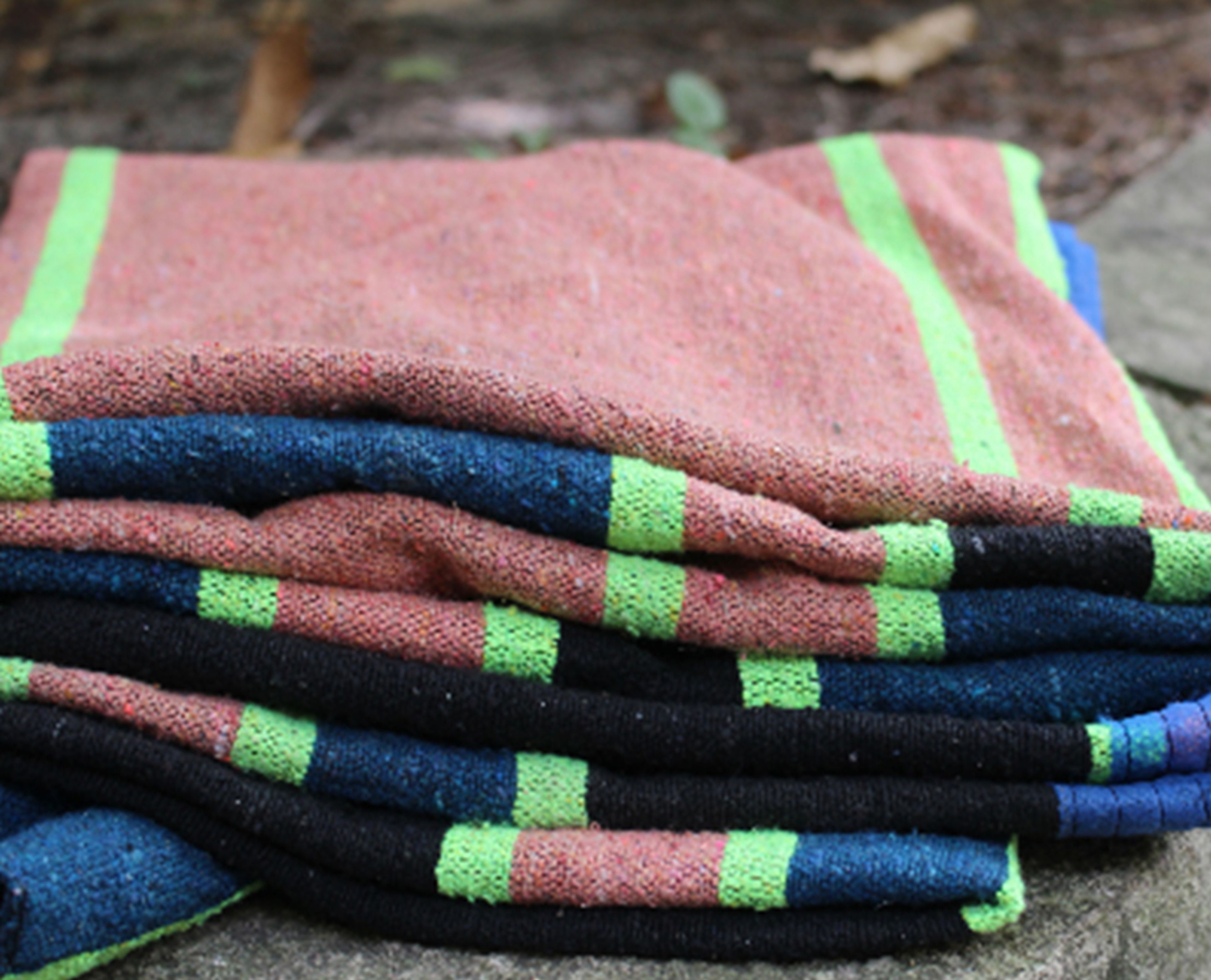 Stack of folded blankets with pink, black, blue, and neon green stripes outdoors.
