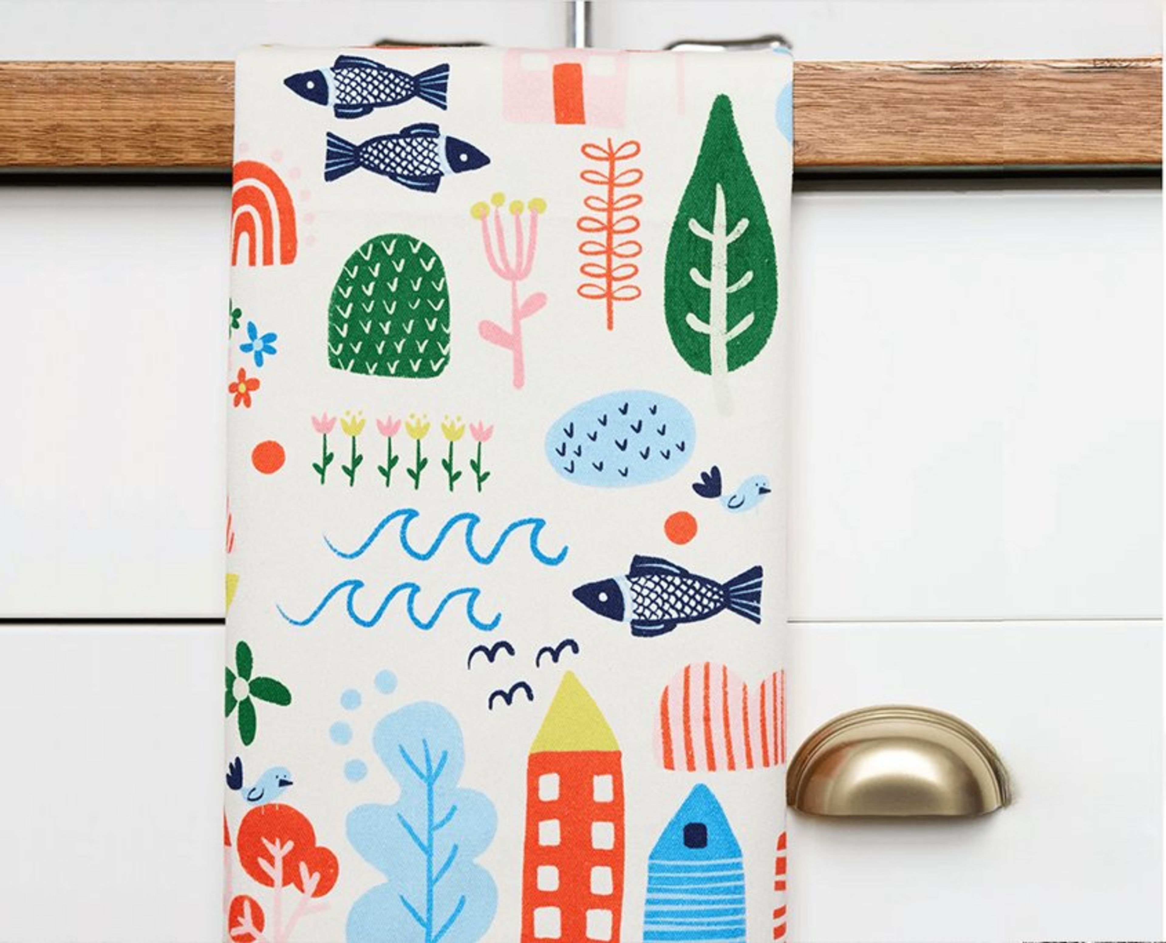 Colorful kitchen towel with whimsical illustrations of fish, plants, houses, and nature motifs.