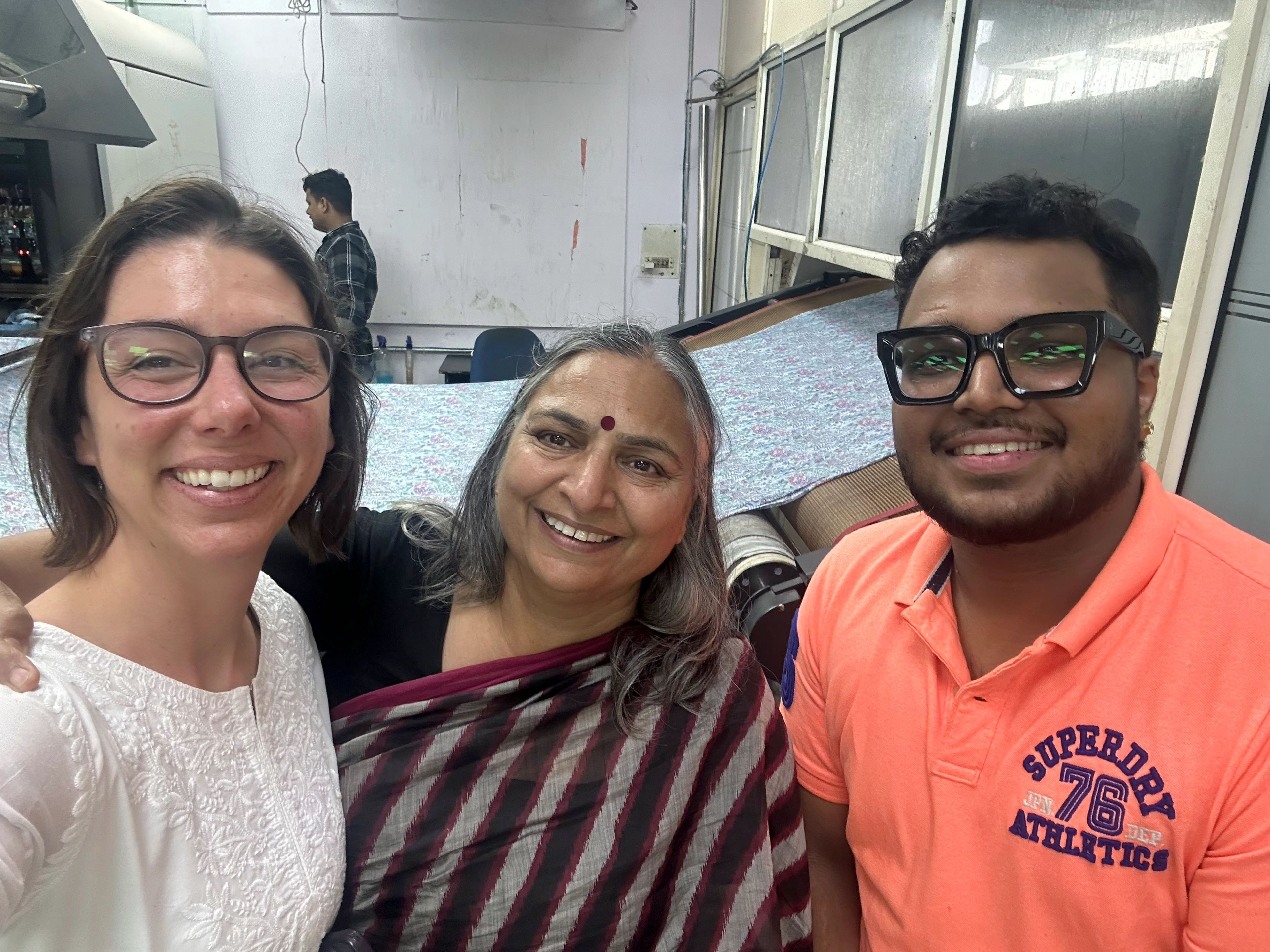 Three smiling people posing together indoors in what appears to be a classroom or community space.
