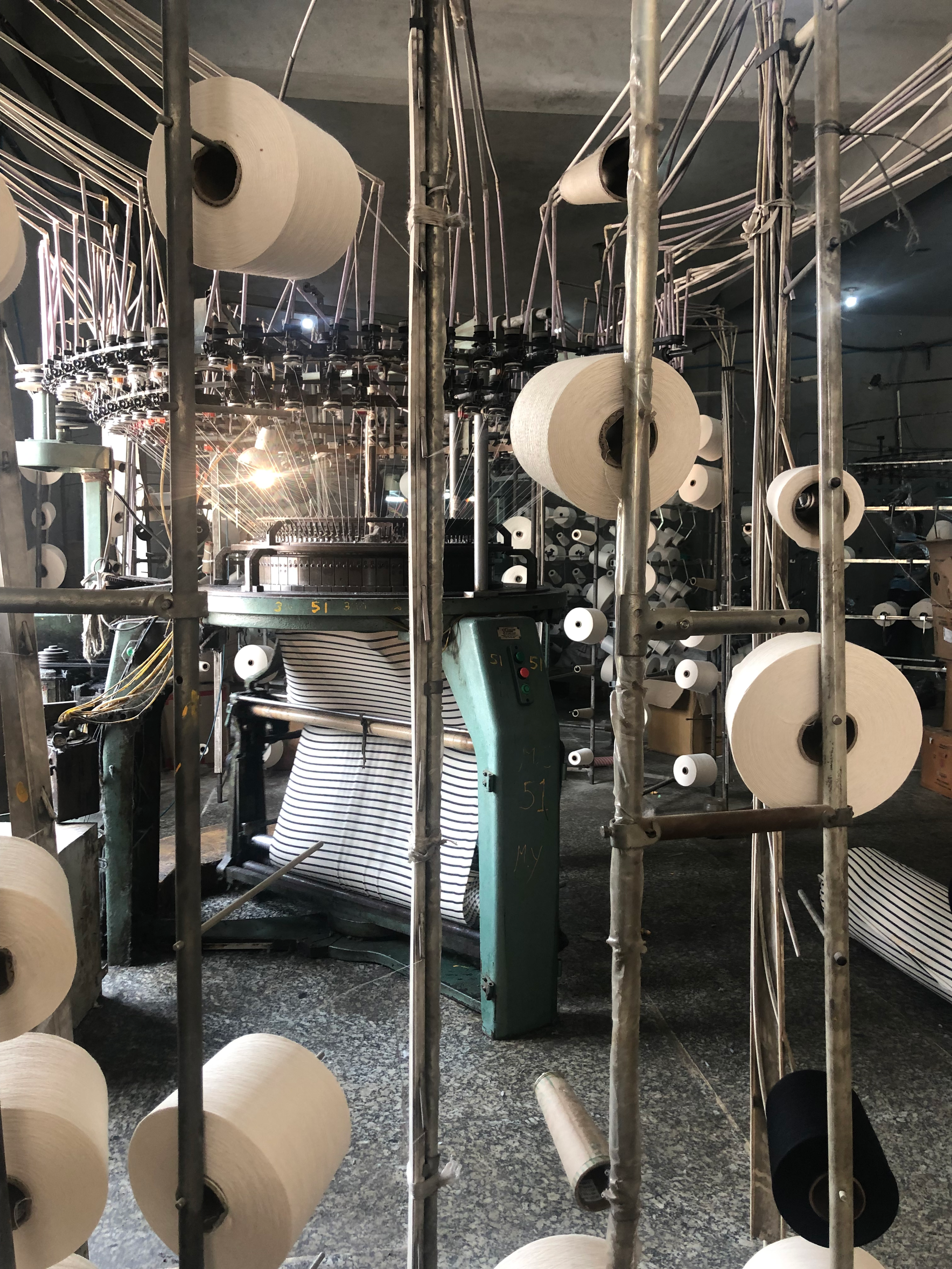 Industrial textile machinery with spools of white thread on metal frames in factory.
