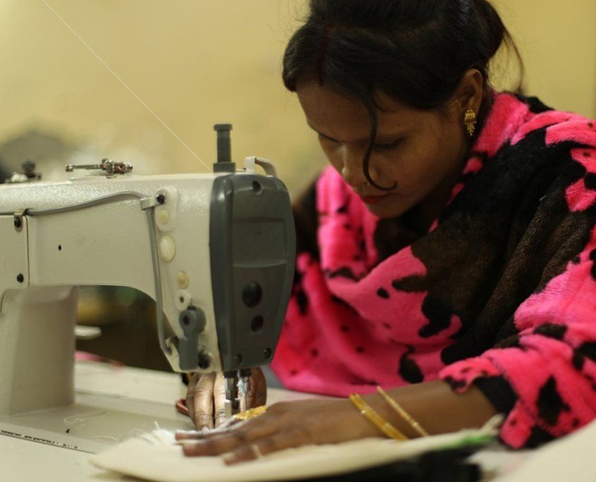Woman in pink and black patterned top sewing fabric on an electric sewing machine.