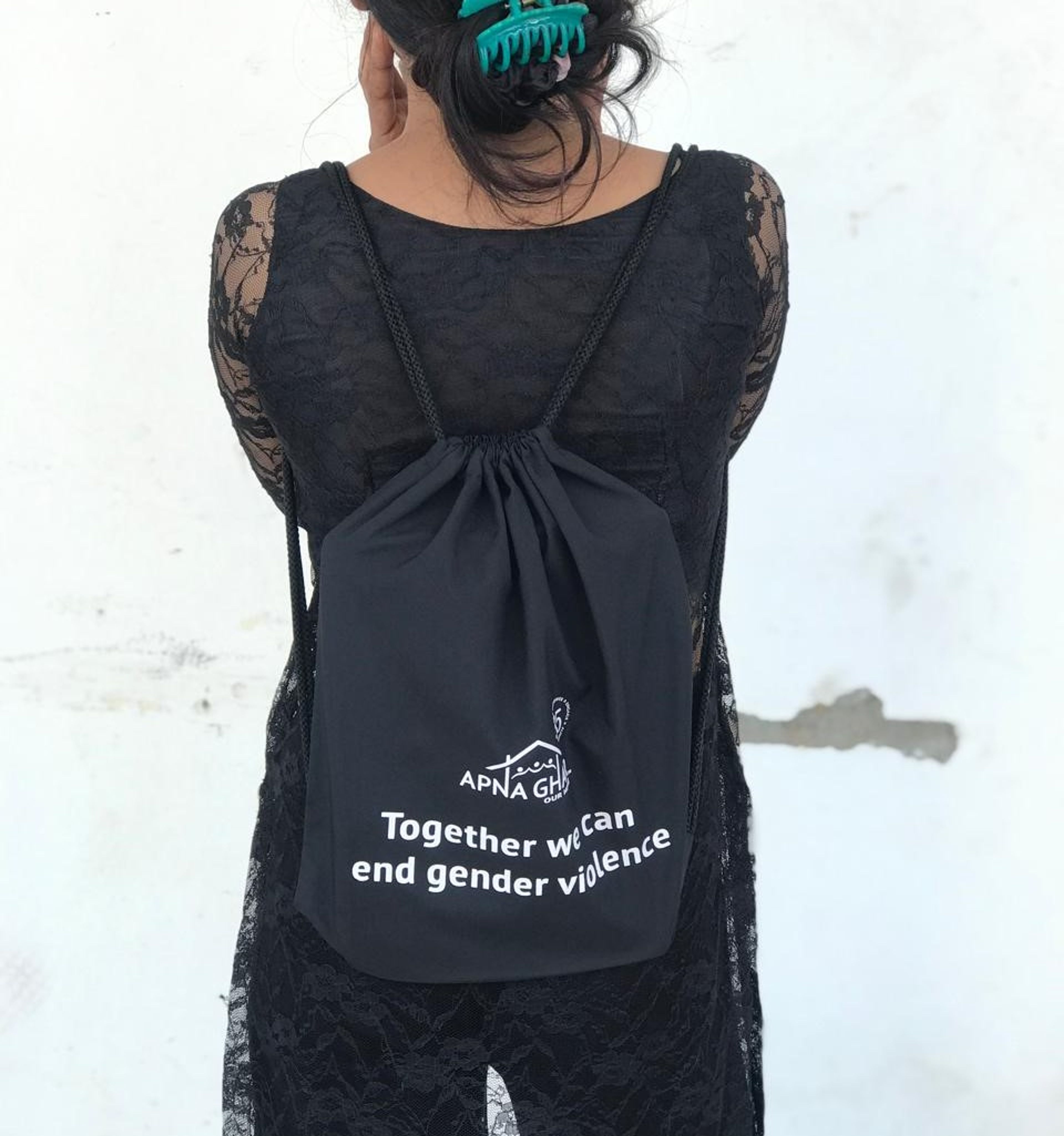 Person wearing black lace dress with "Together we can end gender violence" backpack at beach.
