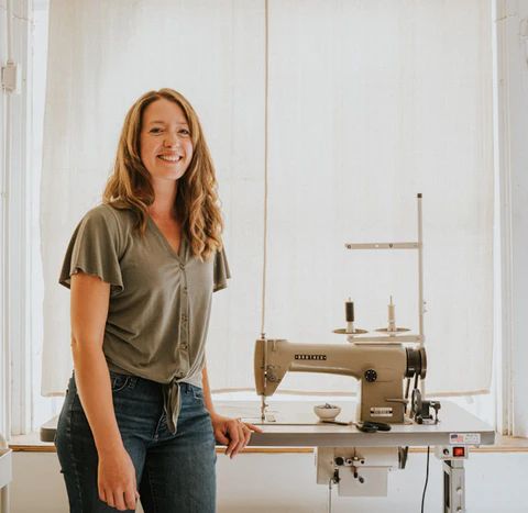 Woman standing beside vintage sewing machine at bright workbench in studio.