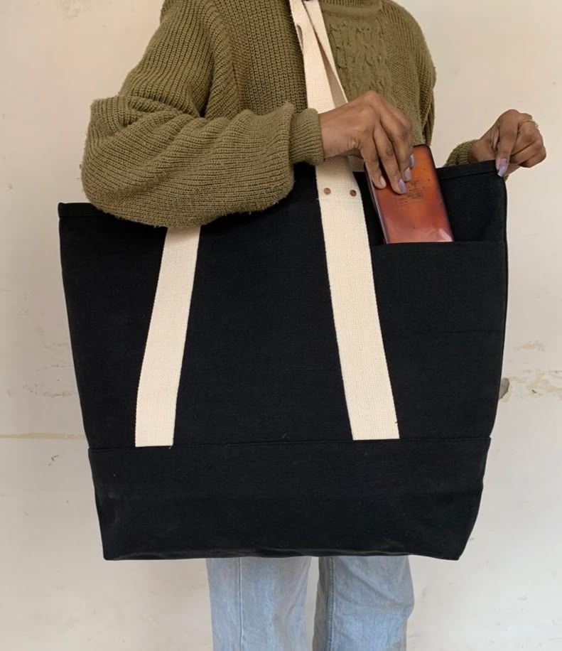 Person holding black canvas tote bag with white handles and brown leather wallet.