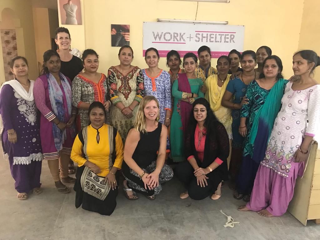 Group photo of women at Work+Shelter organization, standing together in community center room.