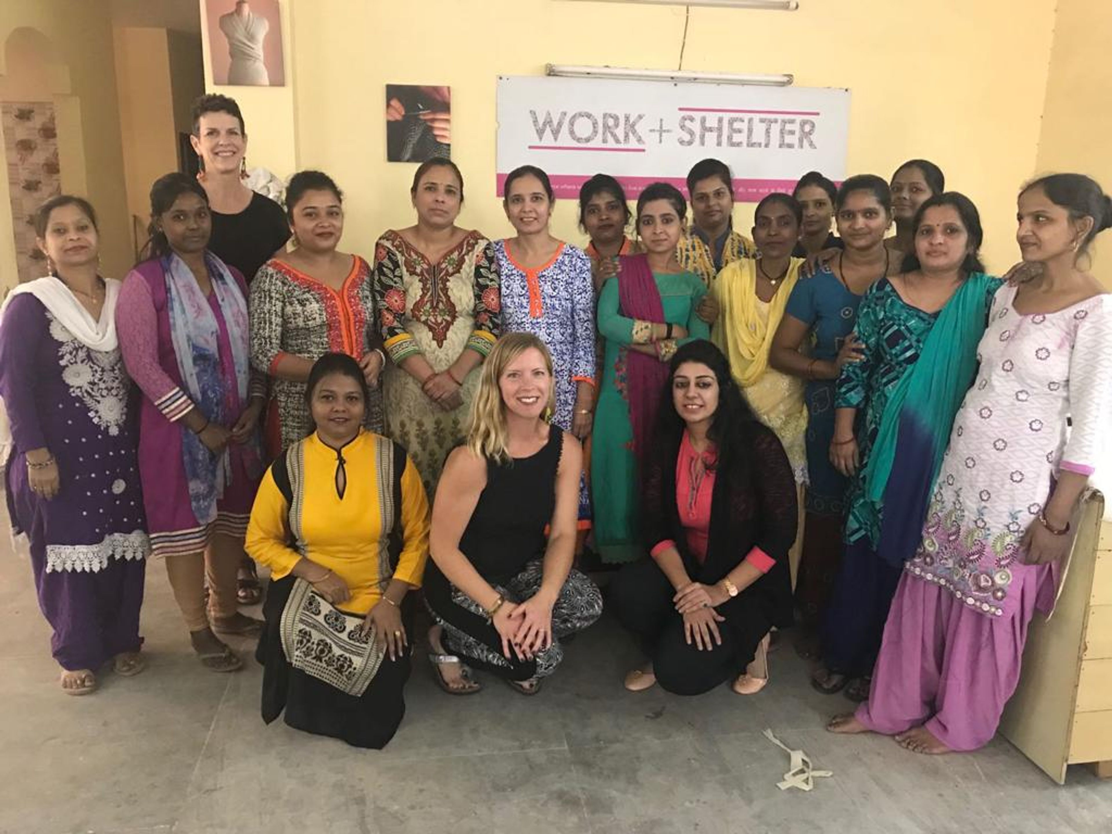 Group photo of women at Work+Shelter organization, standing together in community center room.
