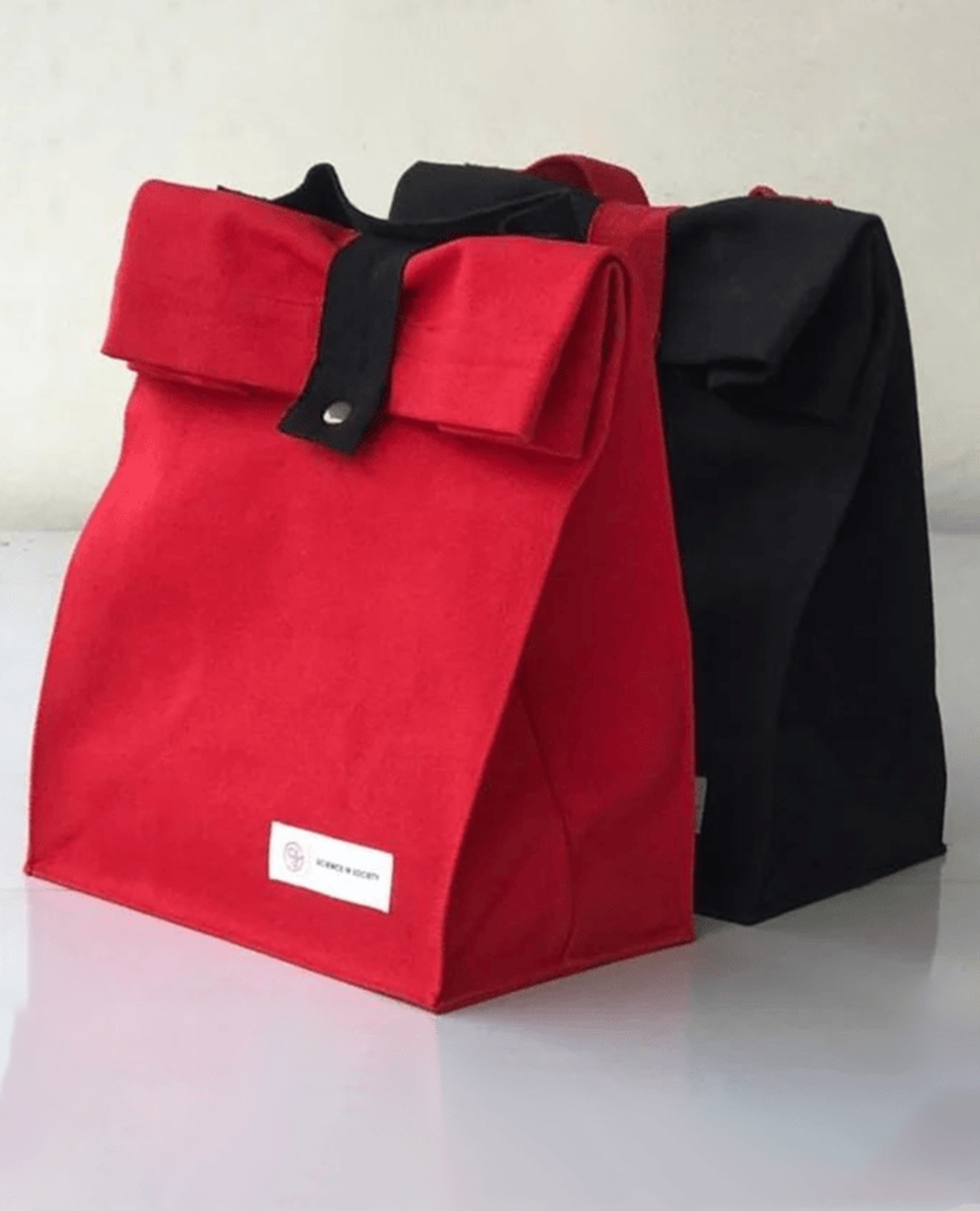 Two canvas lunch Bags in red and black standing upright on a white table