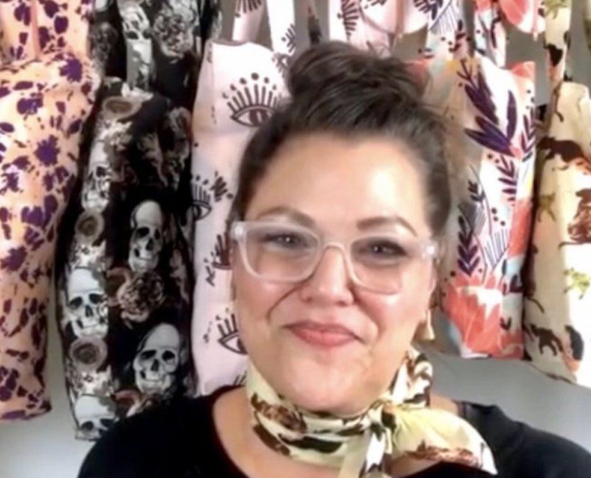 Woman wearing glasses and yellow bandana in fabric store with patterned textiles.