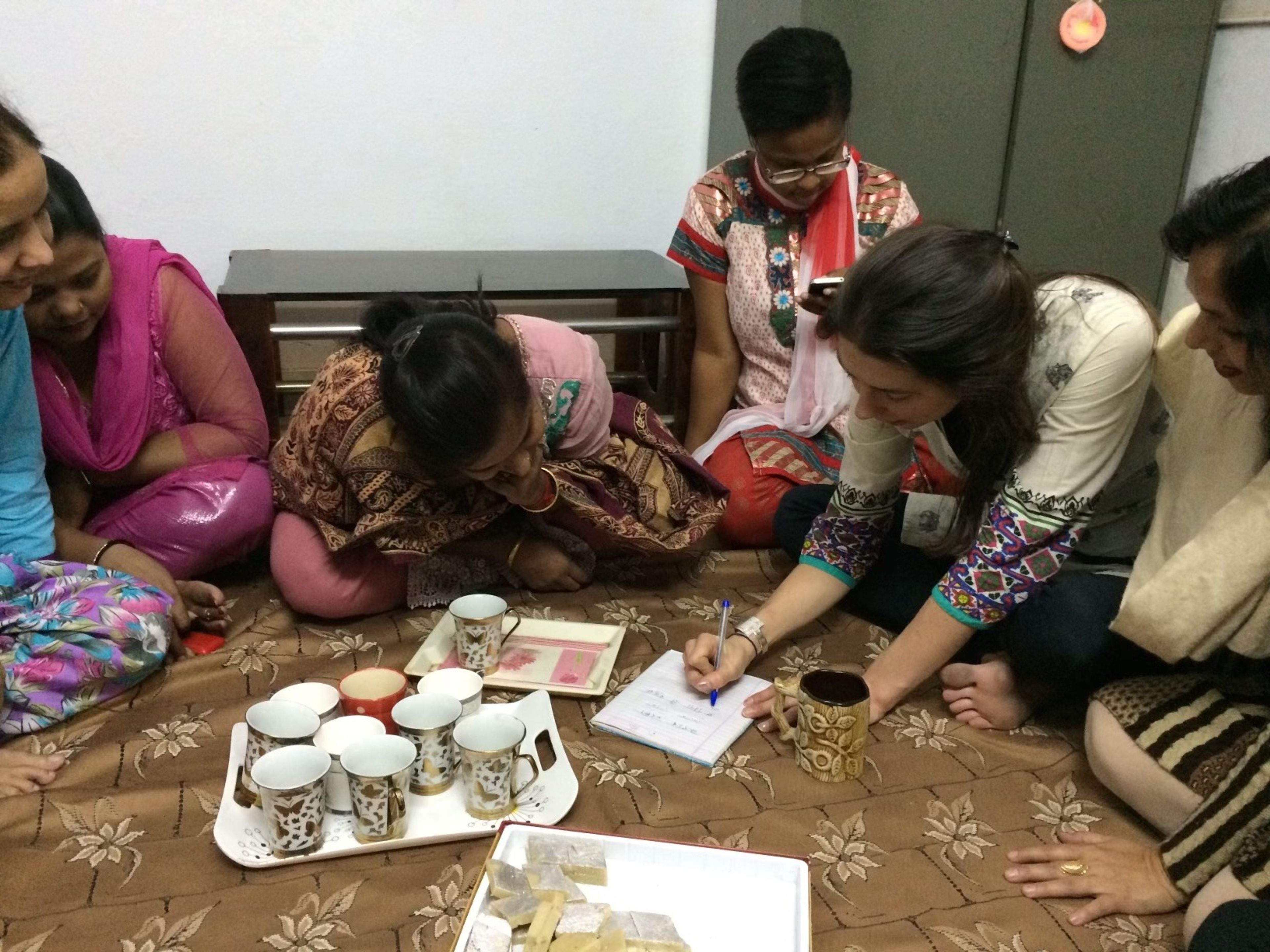 Group of women gathered on floor around documents and tea cups for discussion.