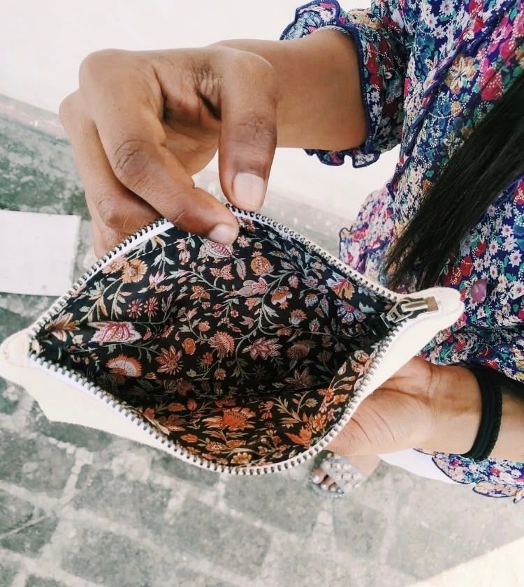 Person holding open a floral-patterned pouch with beaded trim outdoors.