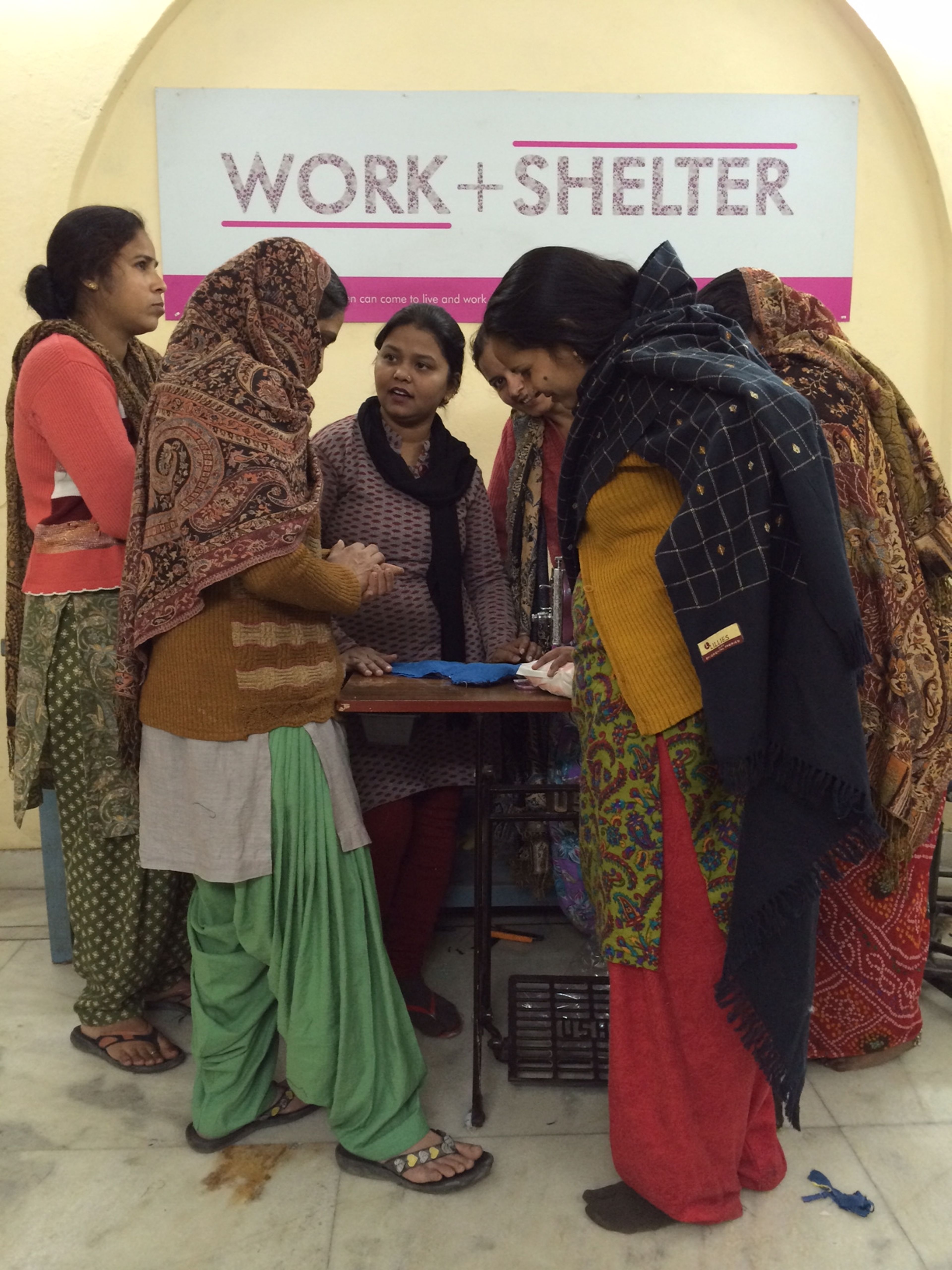 Group of women gathered around table under "Work + Shelter" sign.
