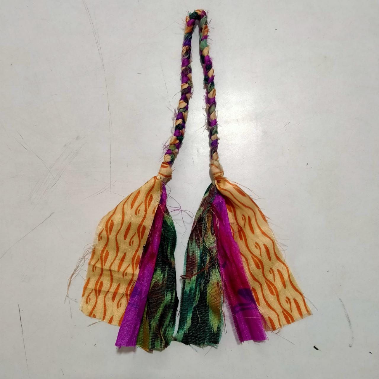 Colorful decorative tassel with braided cord and patterned fabric strips on white background.