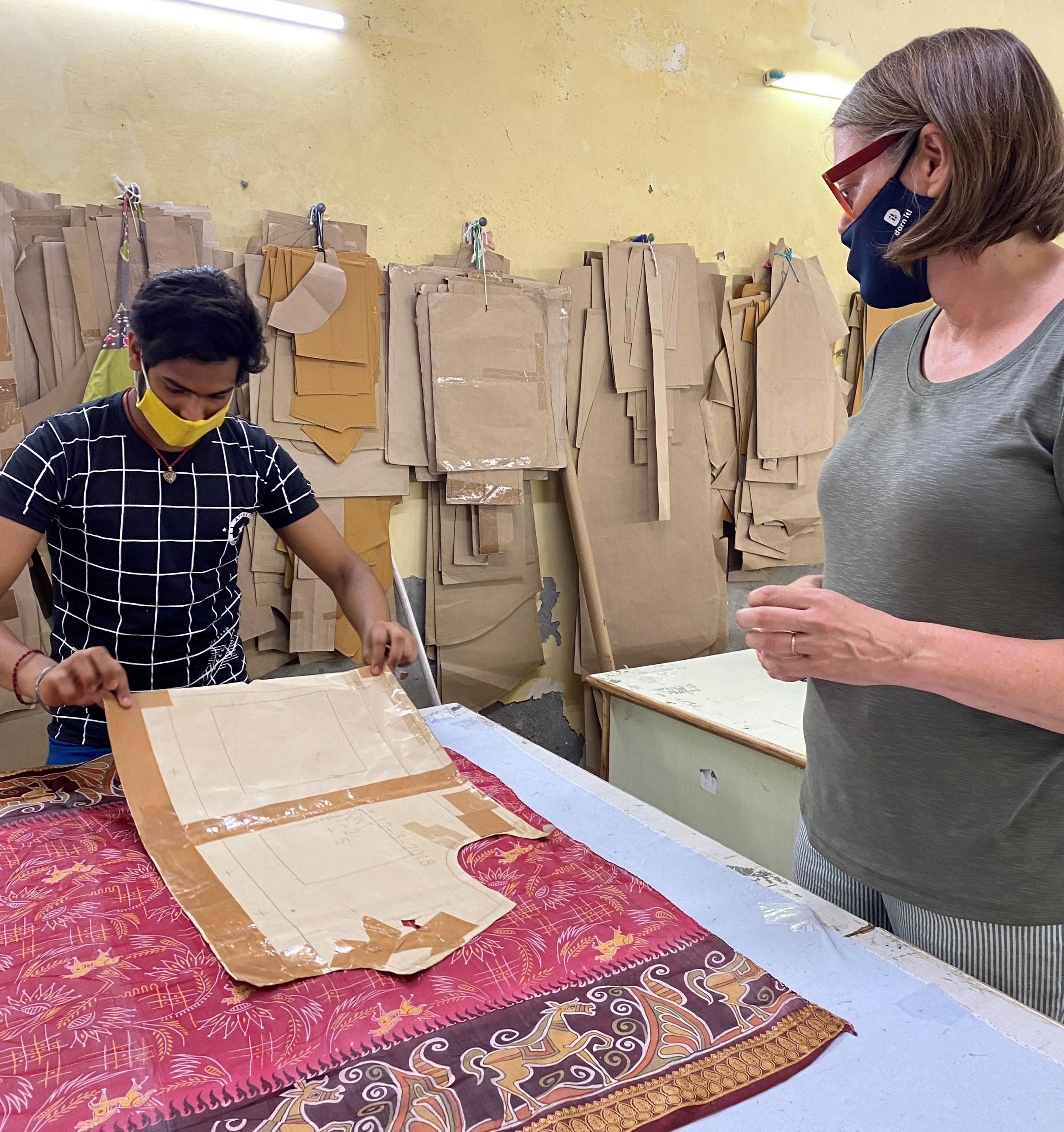 Two people examining textile patterns at work table with fabric samples hanging above.