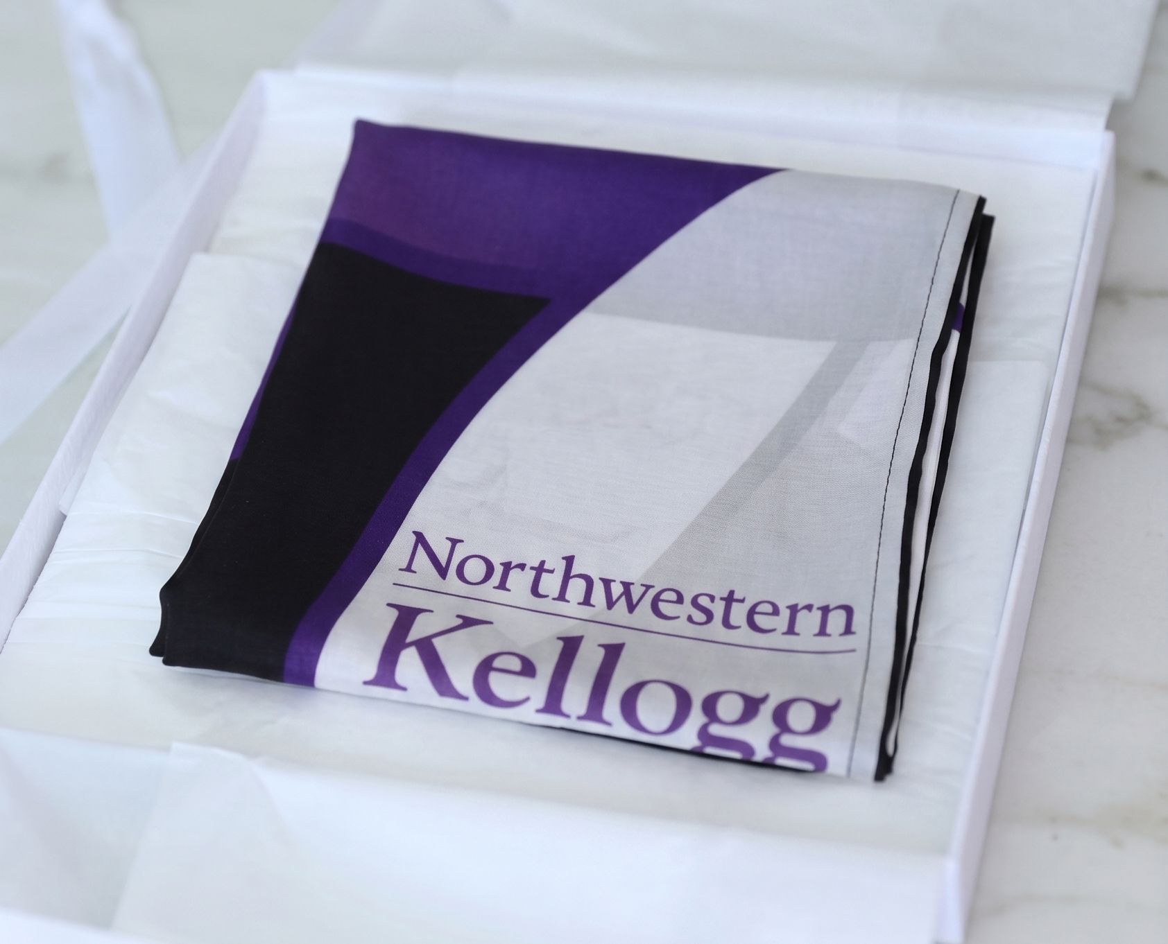 A folded custom-printed silk scarf featuring a geometric stained glass design in purple, black, and white. Design also dis