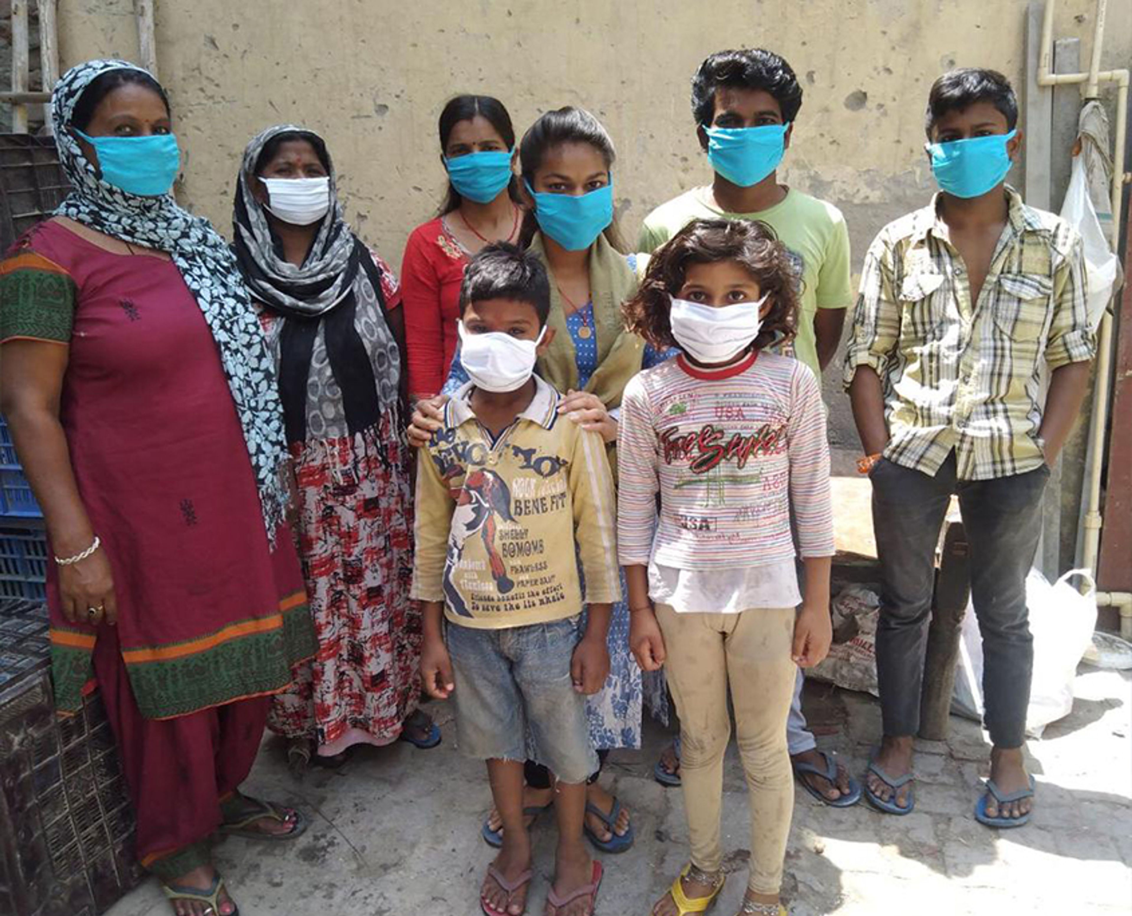 Group of eight people, adults and children, wearing face masks standing together outdoors.