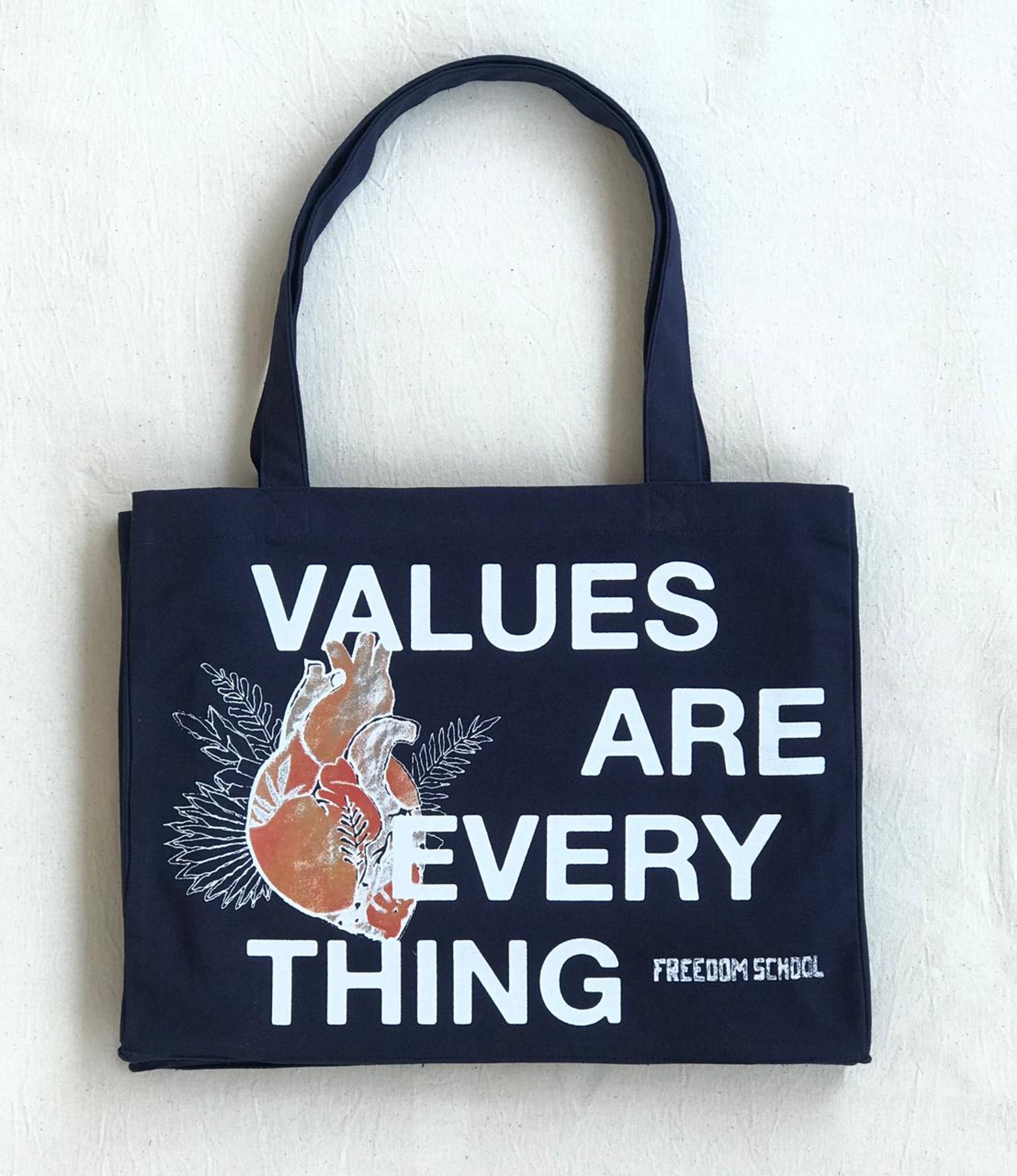 Black tote bag with text "VALUES ARE EVERY THING" and anatomical heart illustration, Freedom School branding.