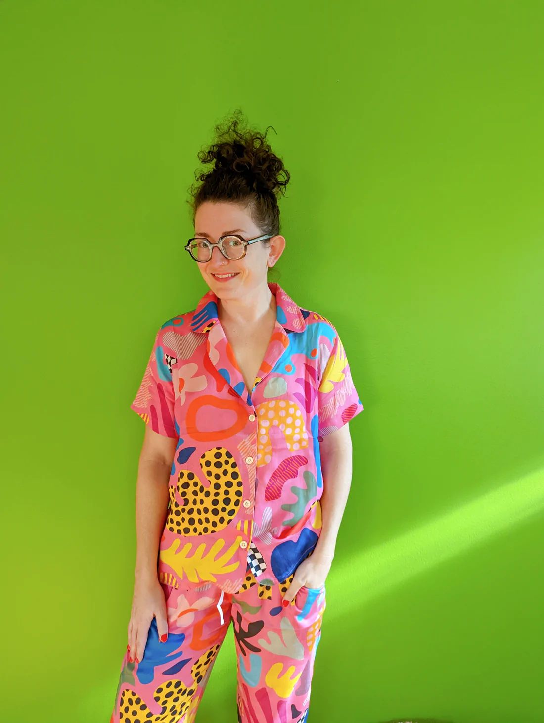Person wearing colorful patterned pajamas and glasses against bright green background.