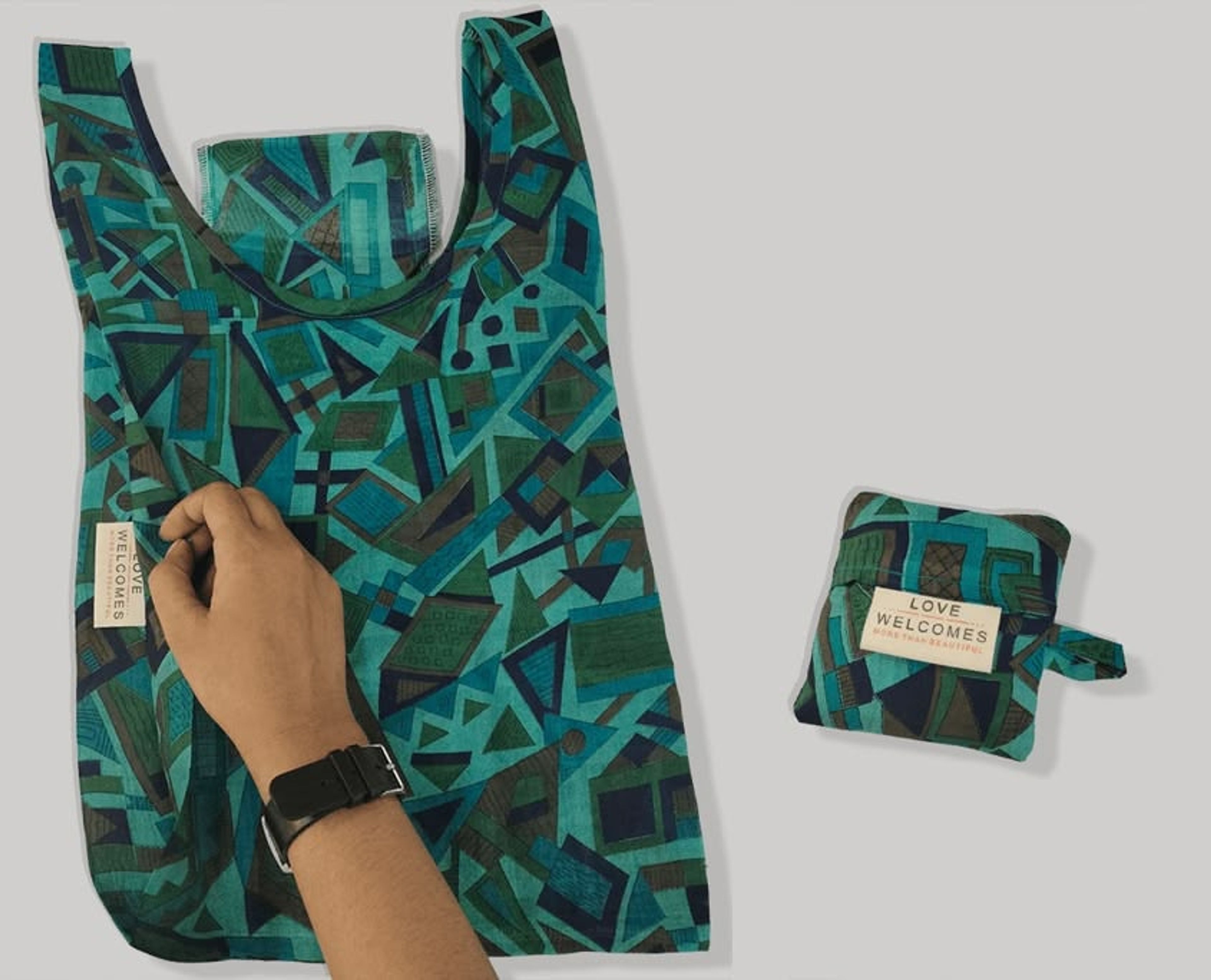 Hand holding teal patterned reusable shopping bag with matching compact folded version displayed.