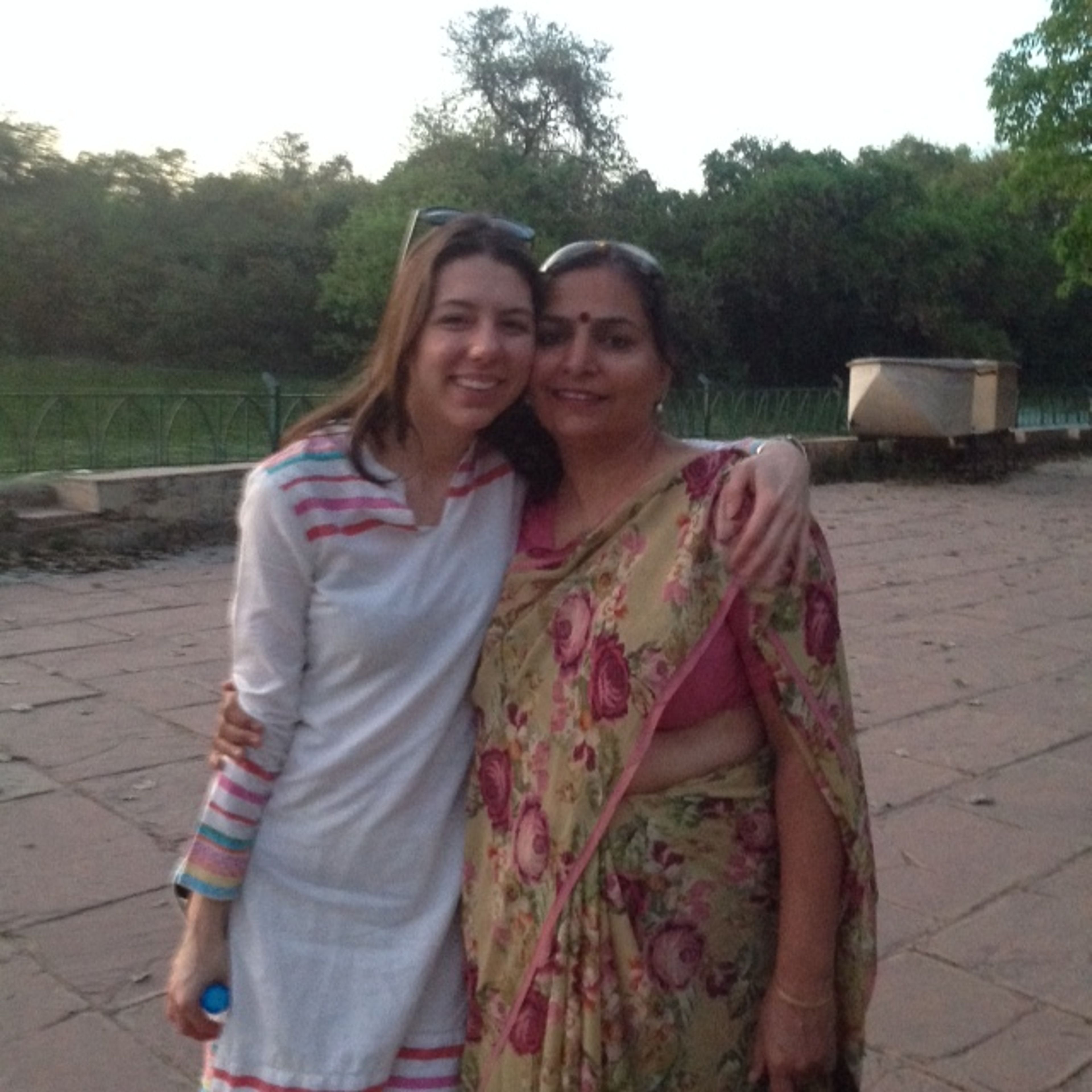 Two women smiling at camera in outdoor courtyard with trees and fencing behind them.