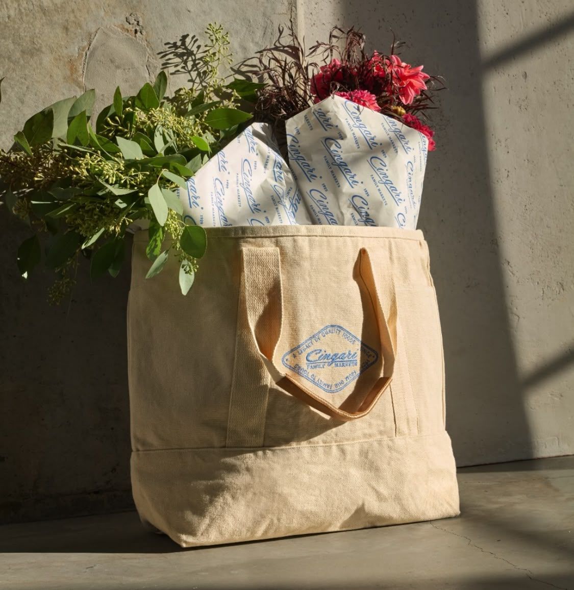 Cream canvas tote bag with flowers and wrapped tissue paper inside, on concrete surface.