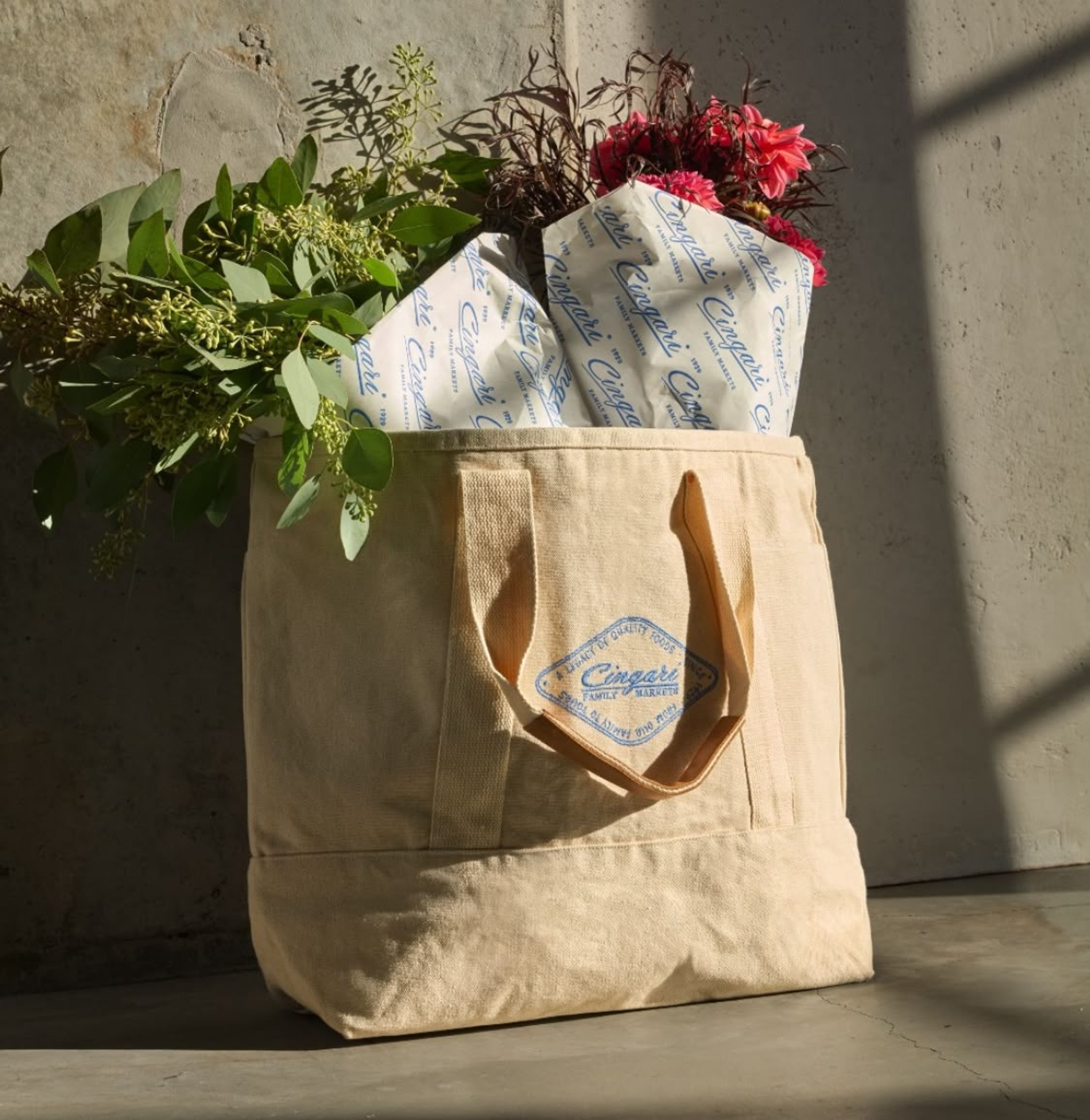 Cream canvas tote bag with flowers and wrapped tissue paper inside, on concrete surface.