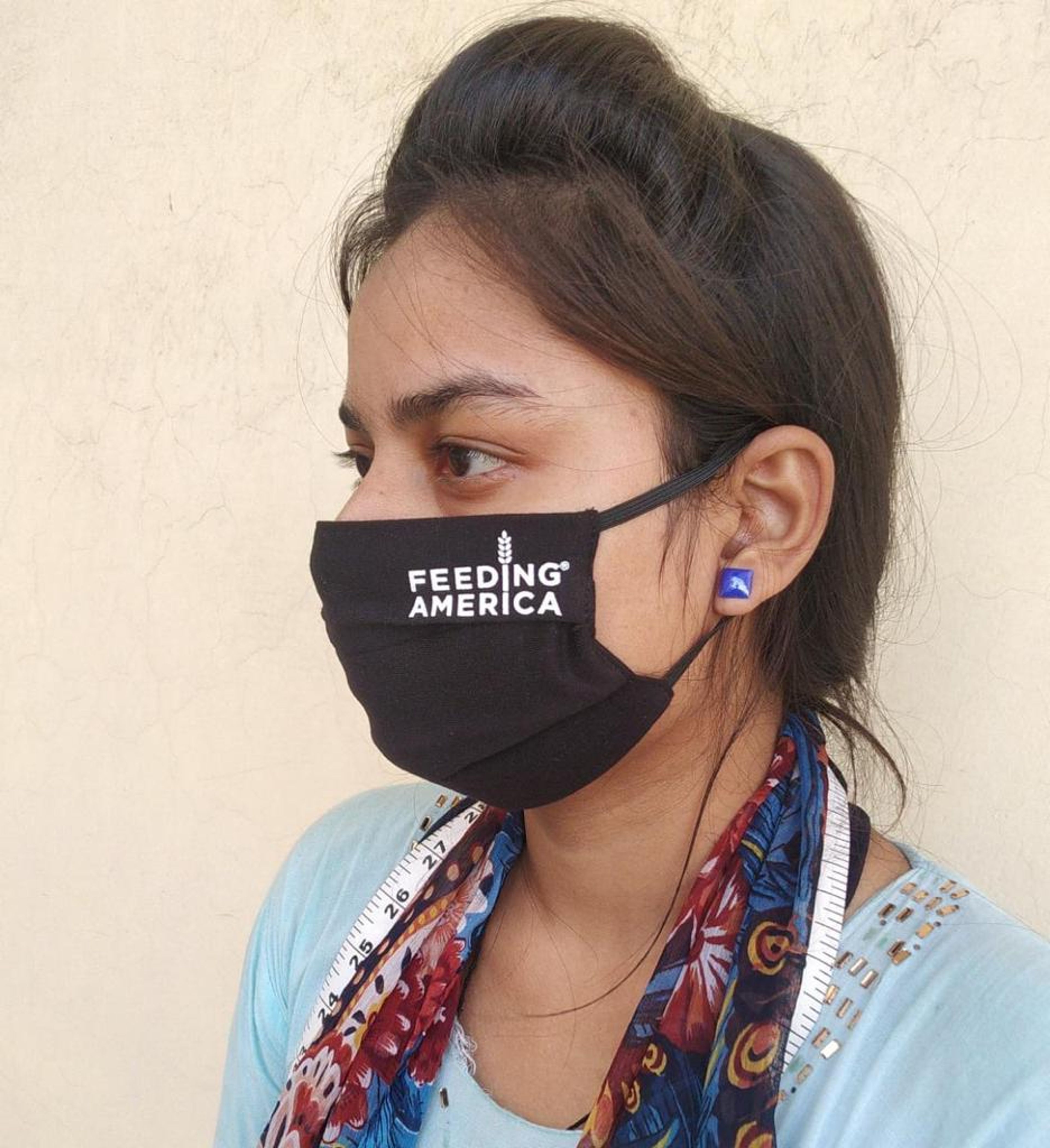 Woman wearing black "Feeding America" face mask and blue earrings, side profile view.
