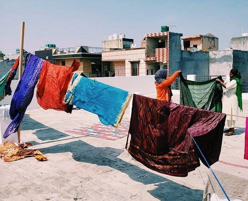 Women hanging colorful fabrics and clothes to dry on rooftop in urban setting.