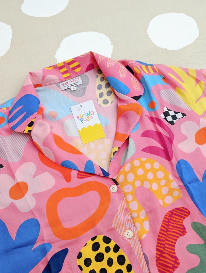 Colorful patterned children's shirt with abstract shapes displayed on cloudy wallpaper background.