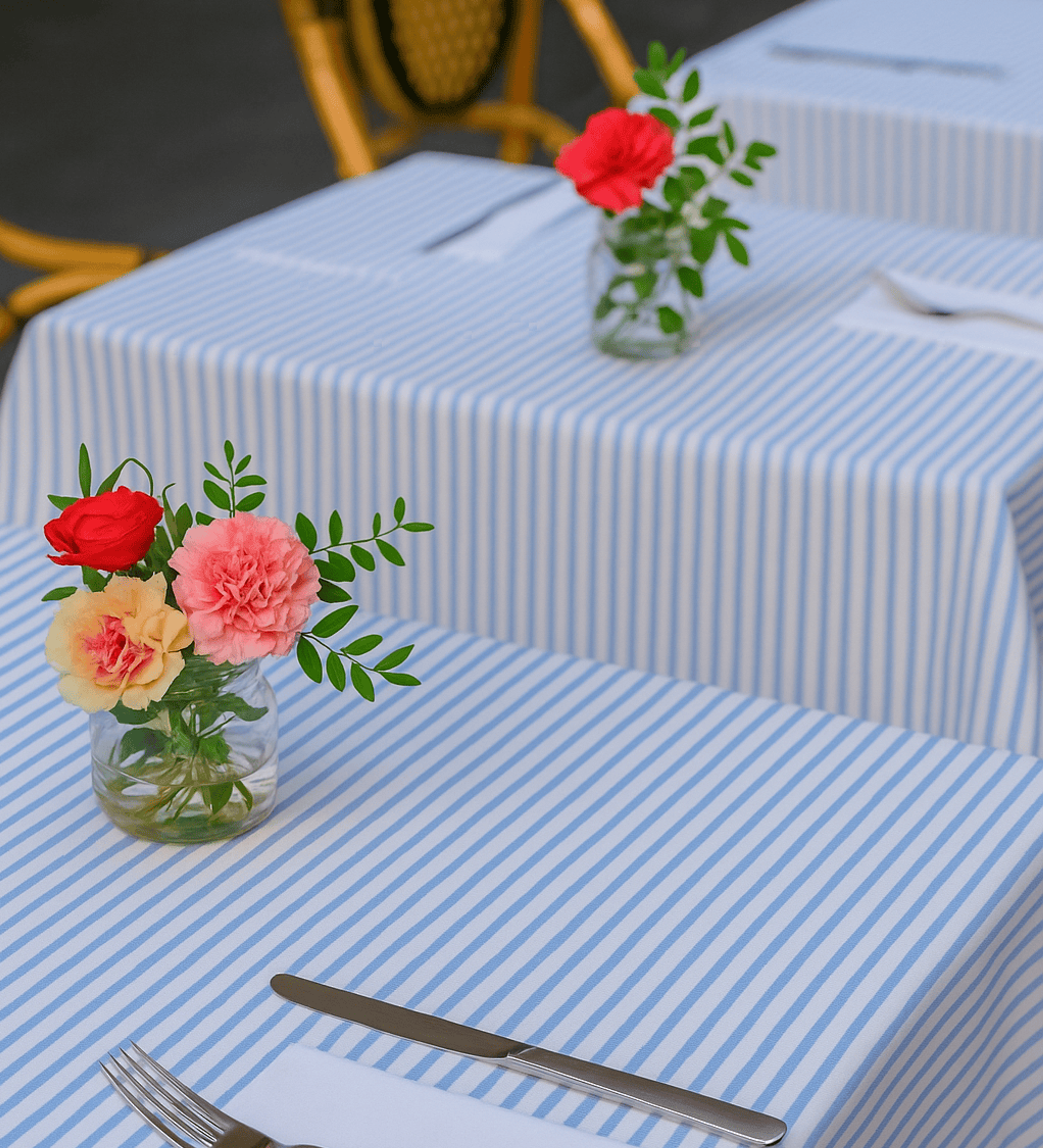 Elegant table setting with blue striped tablecloth, floral centerpieces, and place settings.