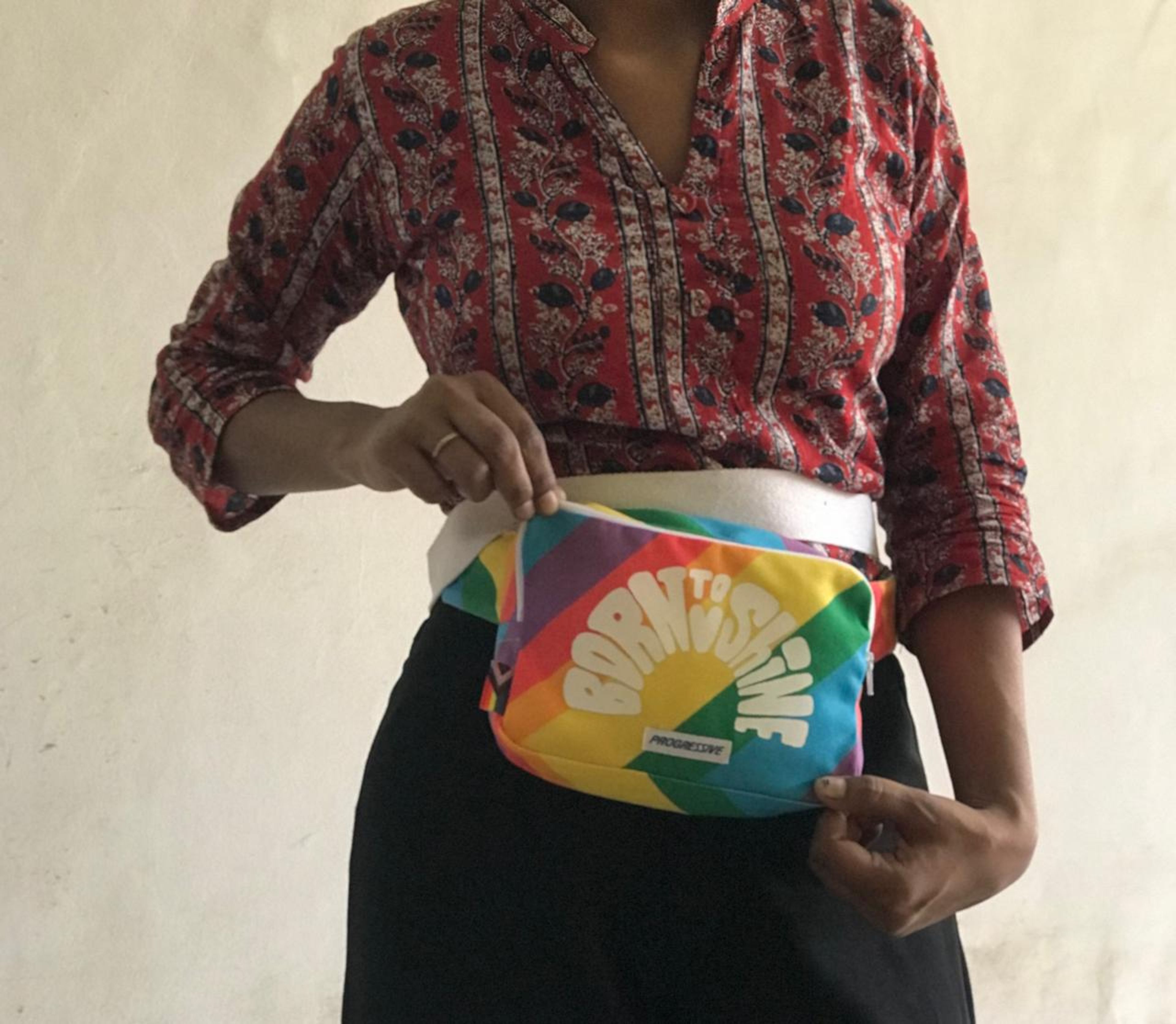 Person wearing red patterned shirt holding colorful rainbow belt bag with "MOTIONWEAR" branding.