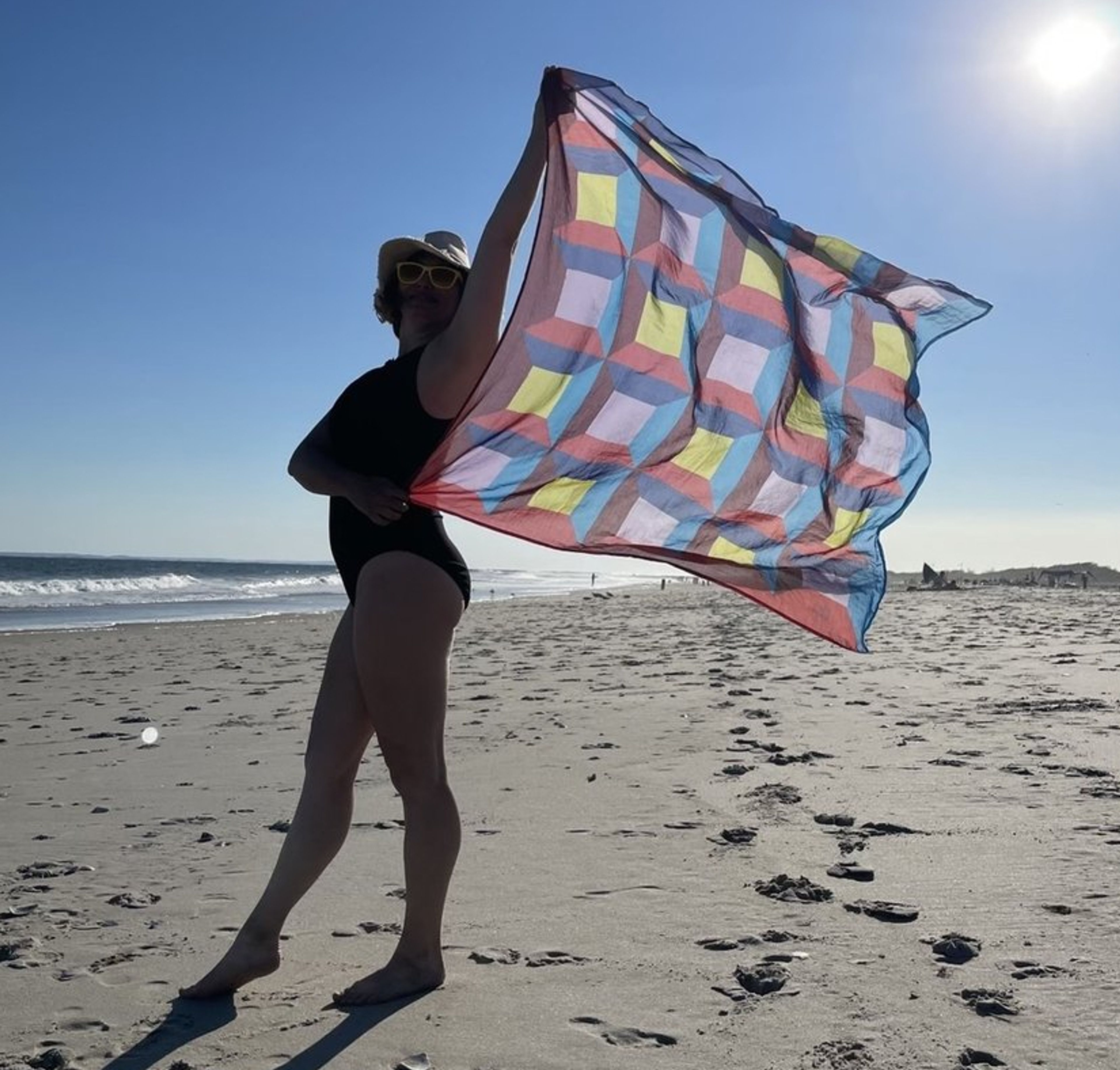 Person holding colorful checkered kite on sandy beach under clear sky.