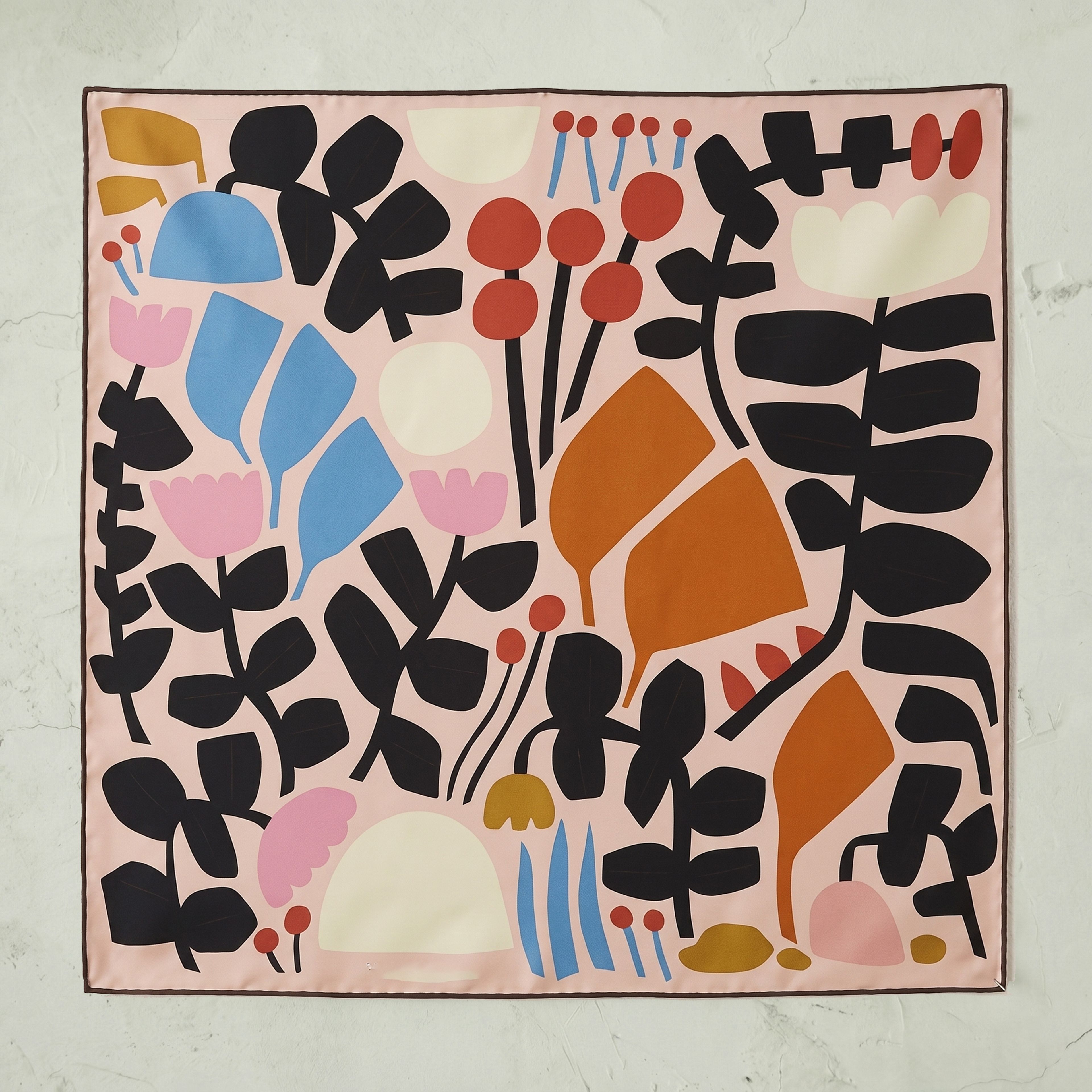 A custom-printed silk scarf featuring a stylized floral design in black, orange, pink, blue, red, white and gold on a pink field.