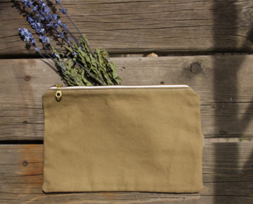 Beige canvas pouch with dried lavender flowers on wooden surface.