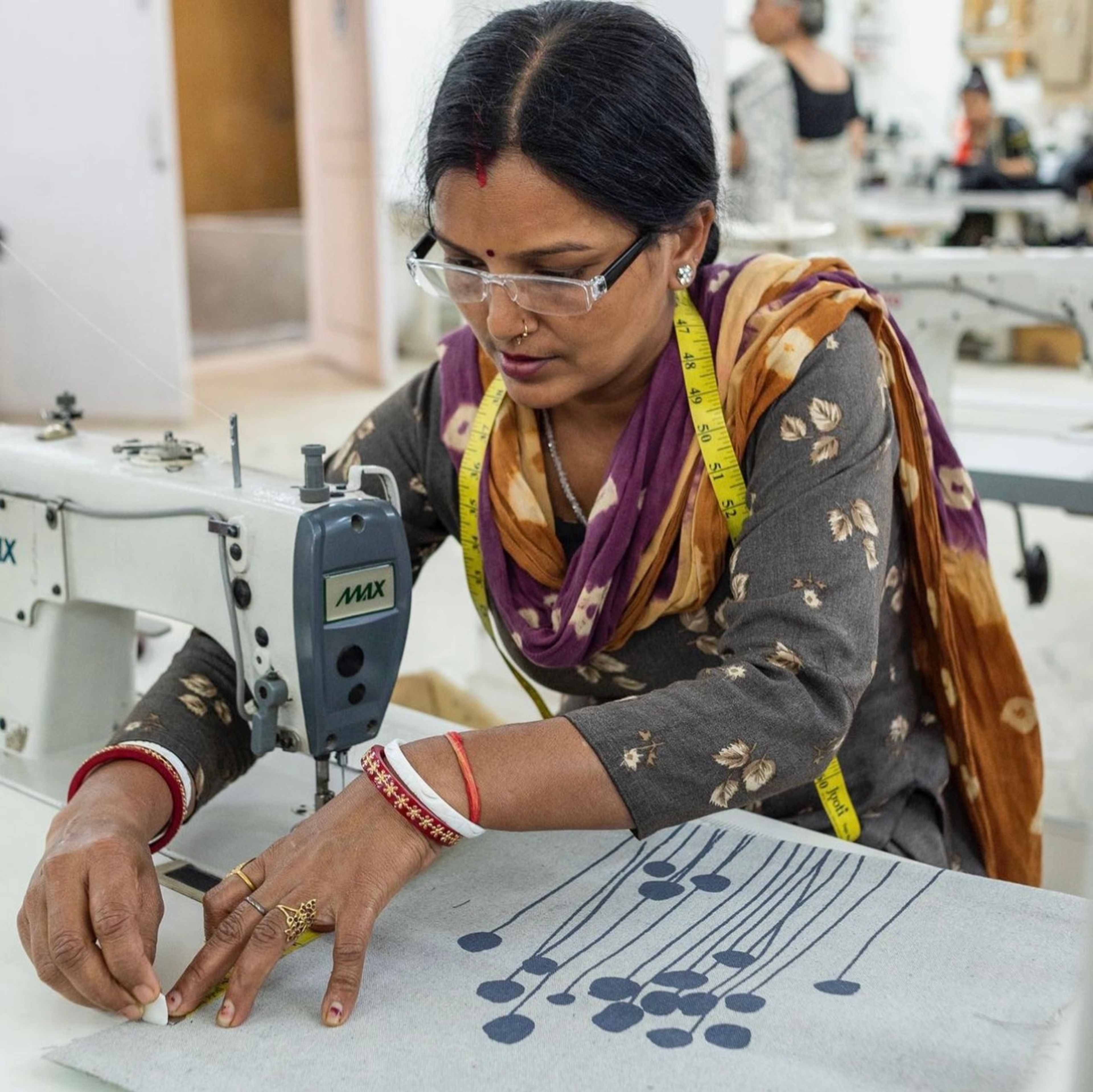Woman using sewing machine to work on patterned fabric in textile workshop.