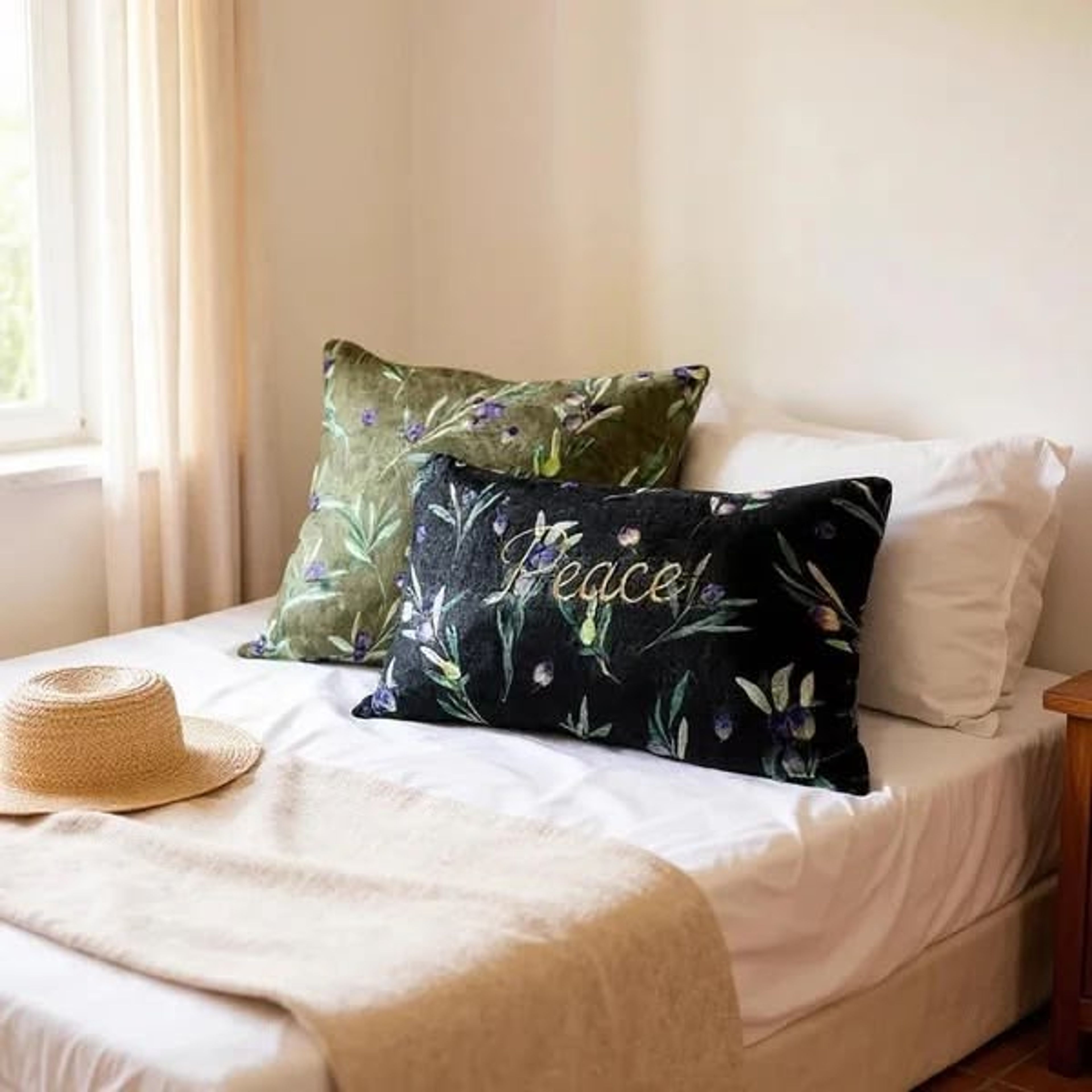 Bed with decorative pillows, straw hat, and white linens near a sunlit window.