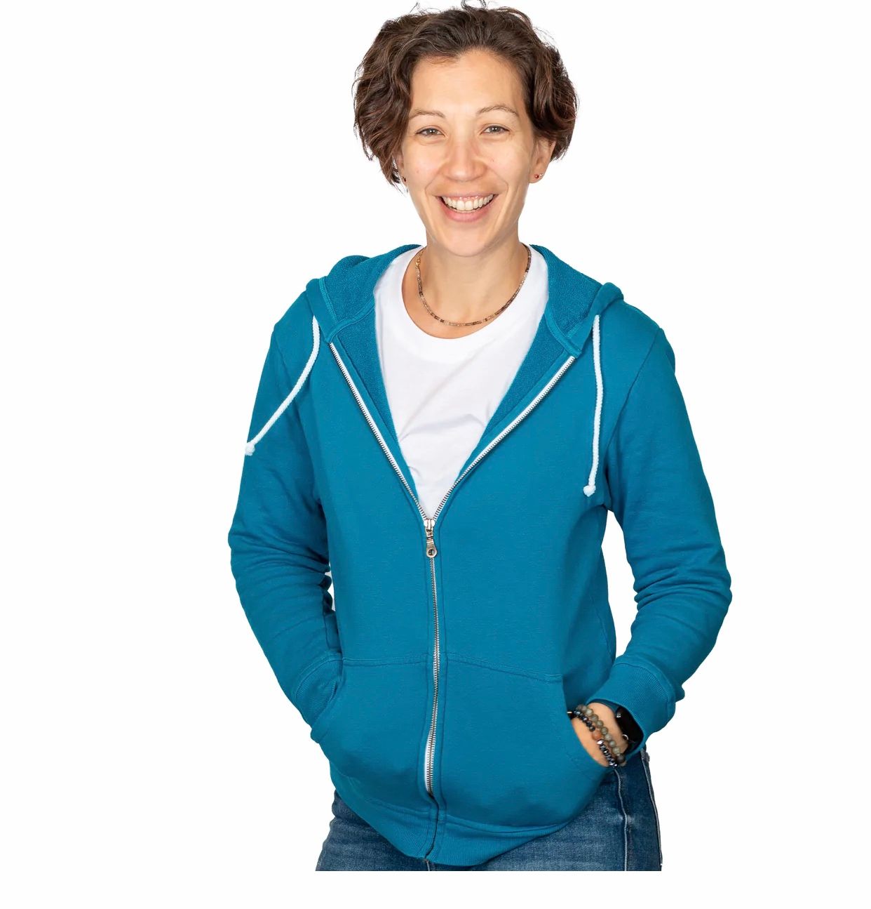 Woman wearing teal zip-up hoodie and white shirt, smiling at camera against white background.