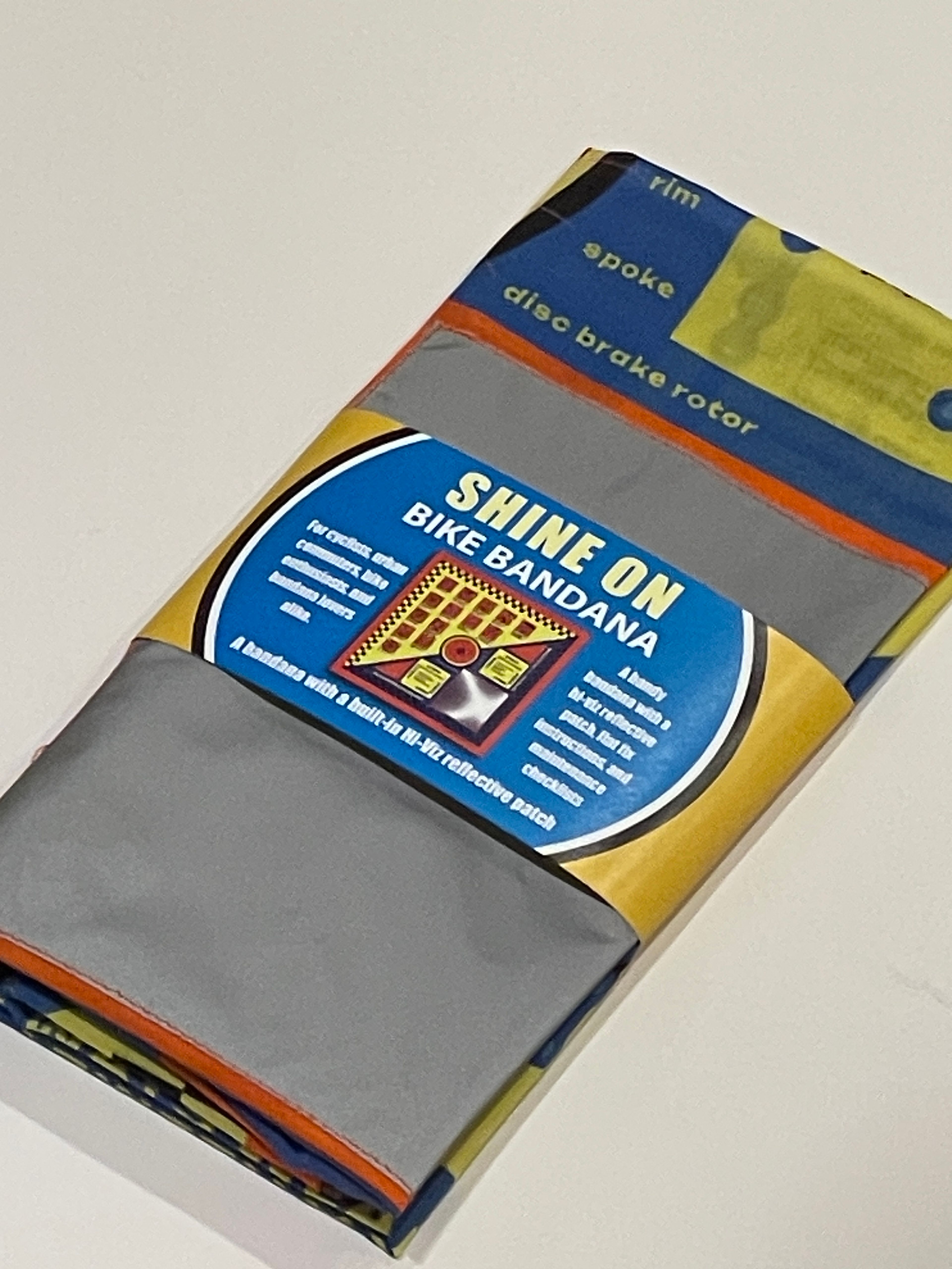 Packaged gray bike bandana with blue "Shine On Bike Bandana" label and colorful striped design.