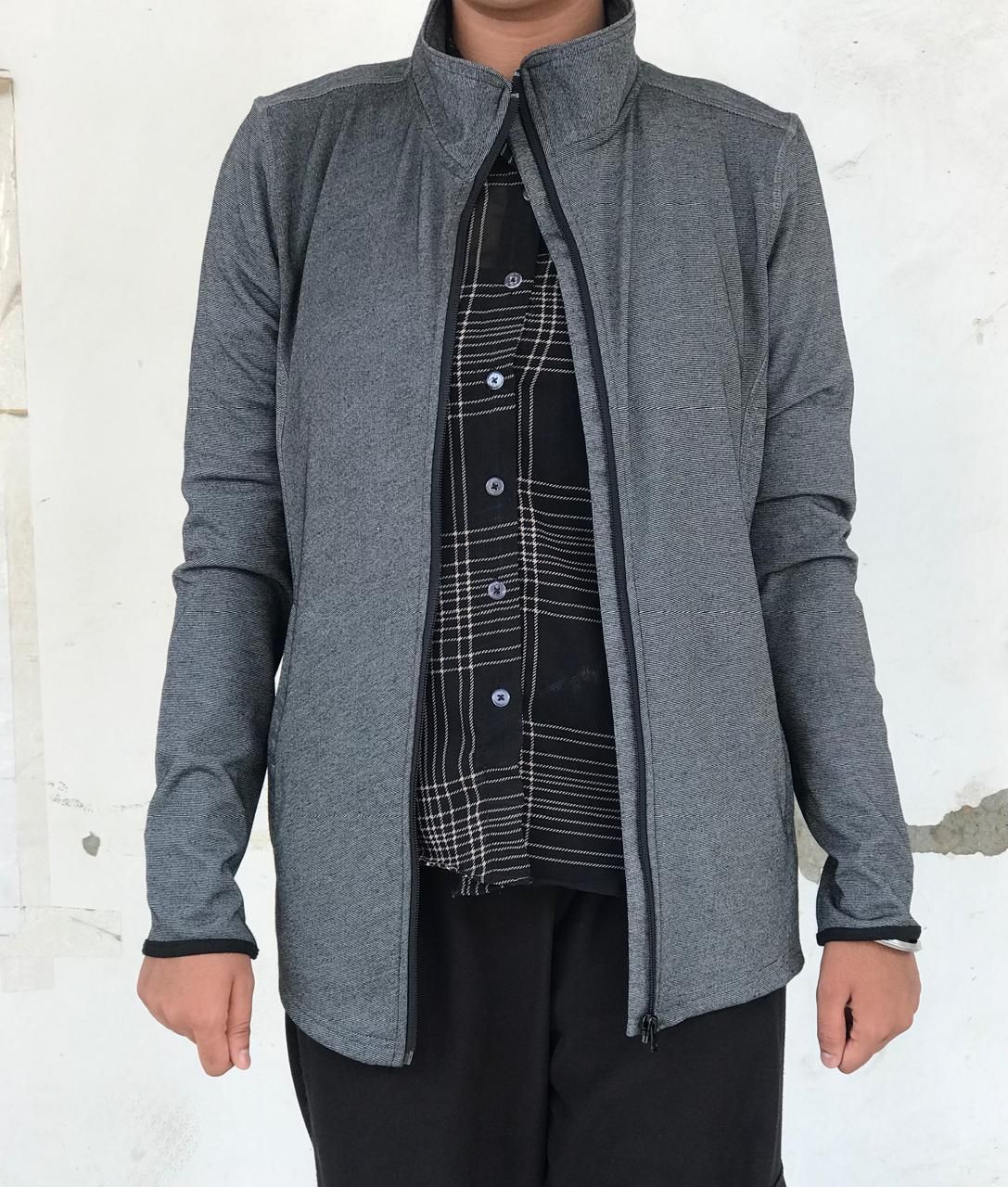 Person wearing gray zip-up jacket over plaid shirt and black pants.