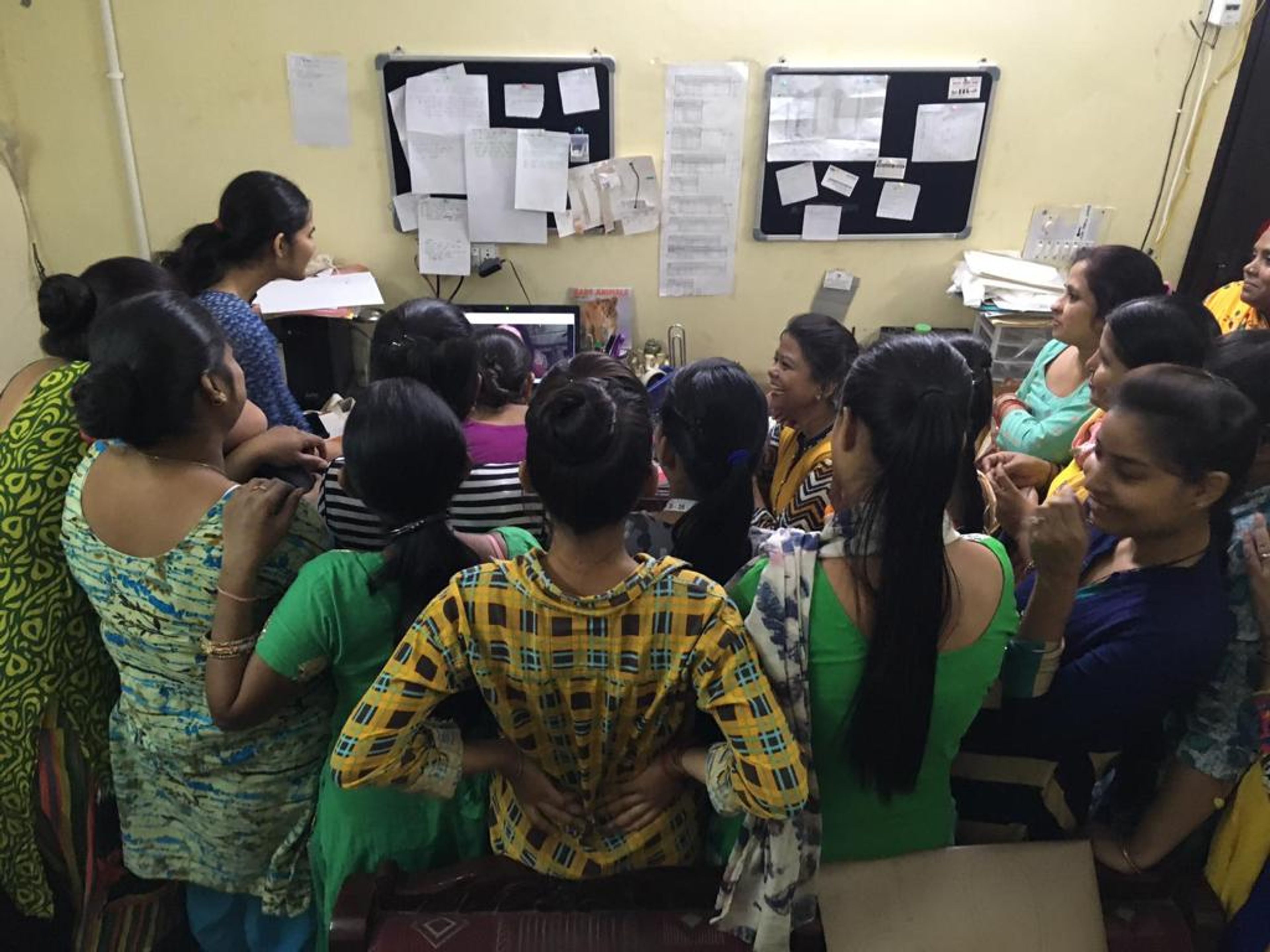 Large group of women gathered in yellow classroom for community meeting or training session.