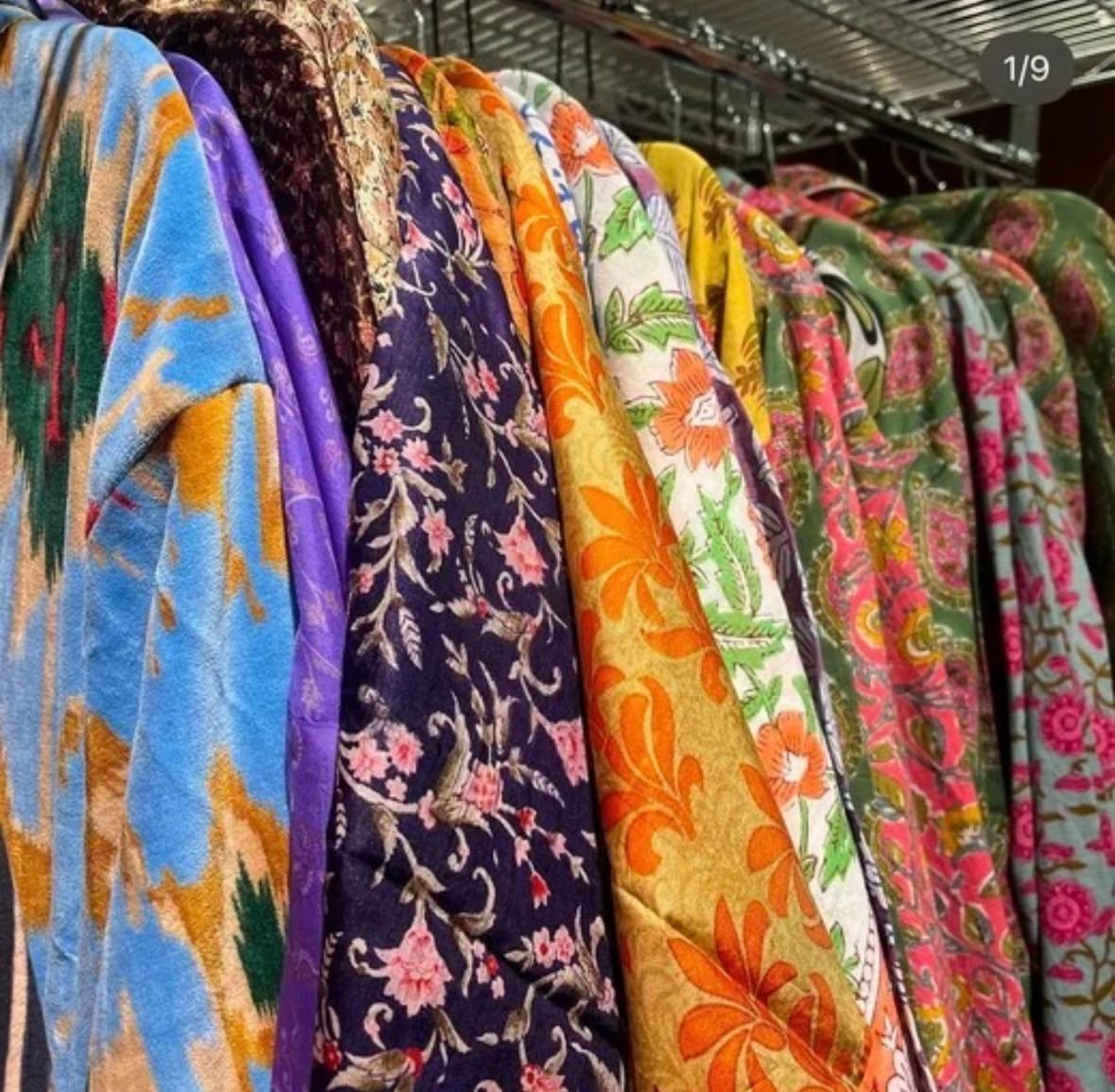 Colorful floral patterned fabrics hanging on display in textile warehouse or market.