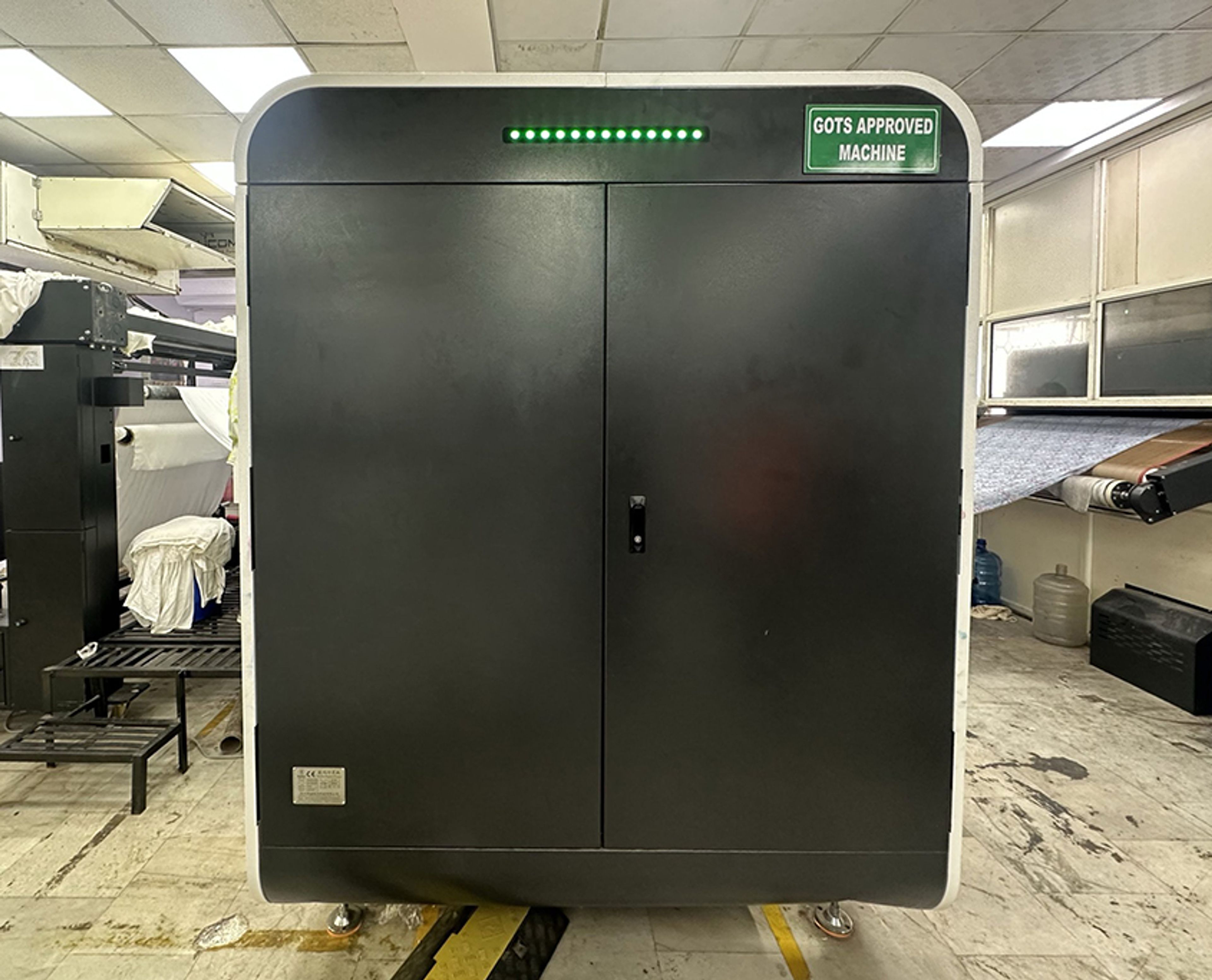 Large black industrial machine labeled "GOTS Approved Machine" in workshop setting.