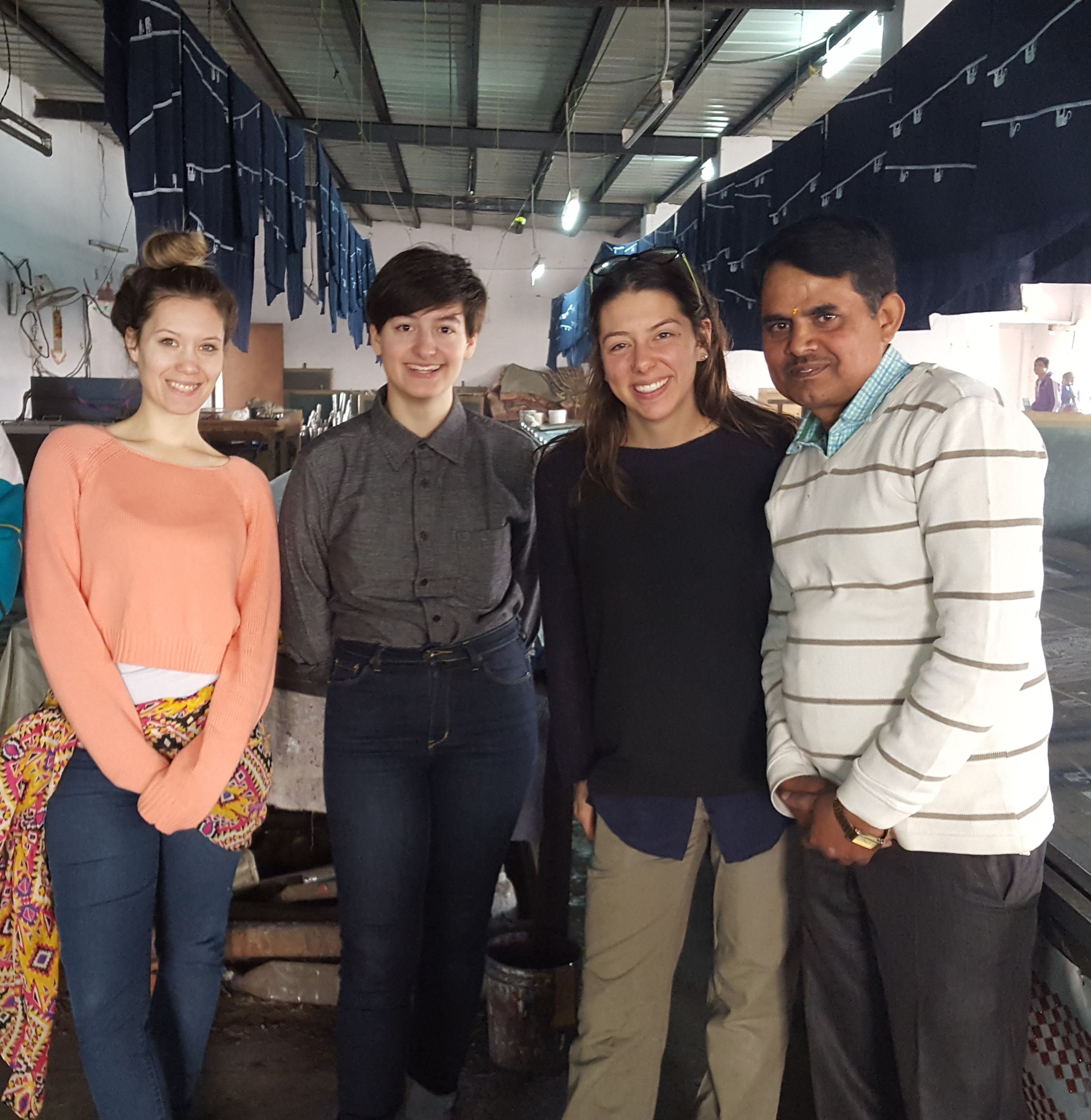 Four smiling people posing together in an industrial warehouse space with hanging fabrics.